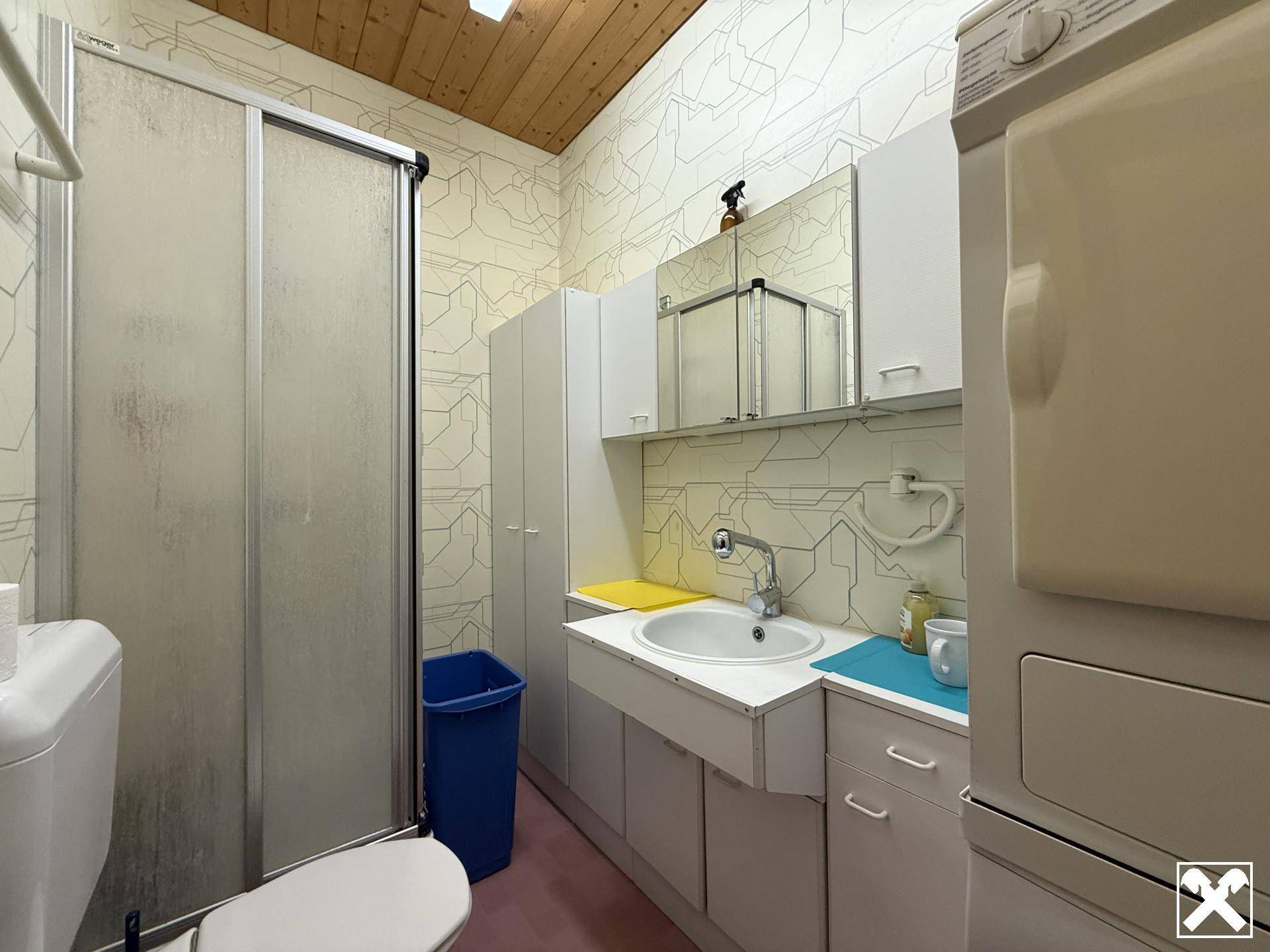 Praktisches Badezimmer mit Duschkabine, Waschbecken, Toilette und Waschmaschine, funktional eingerichtet.