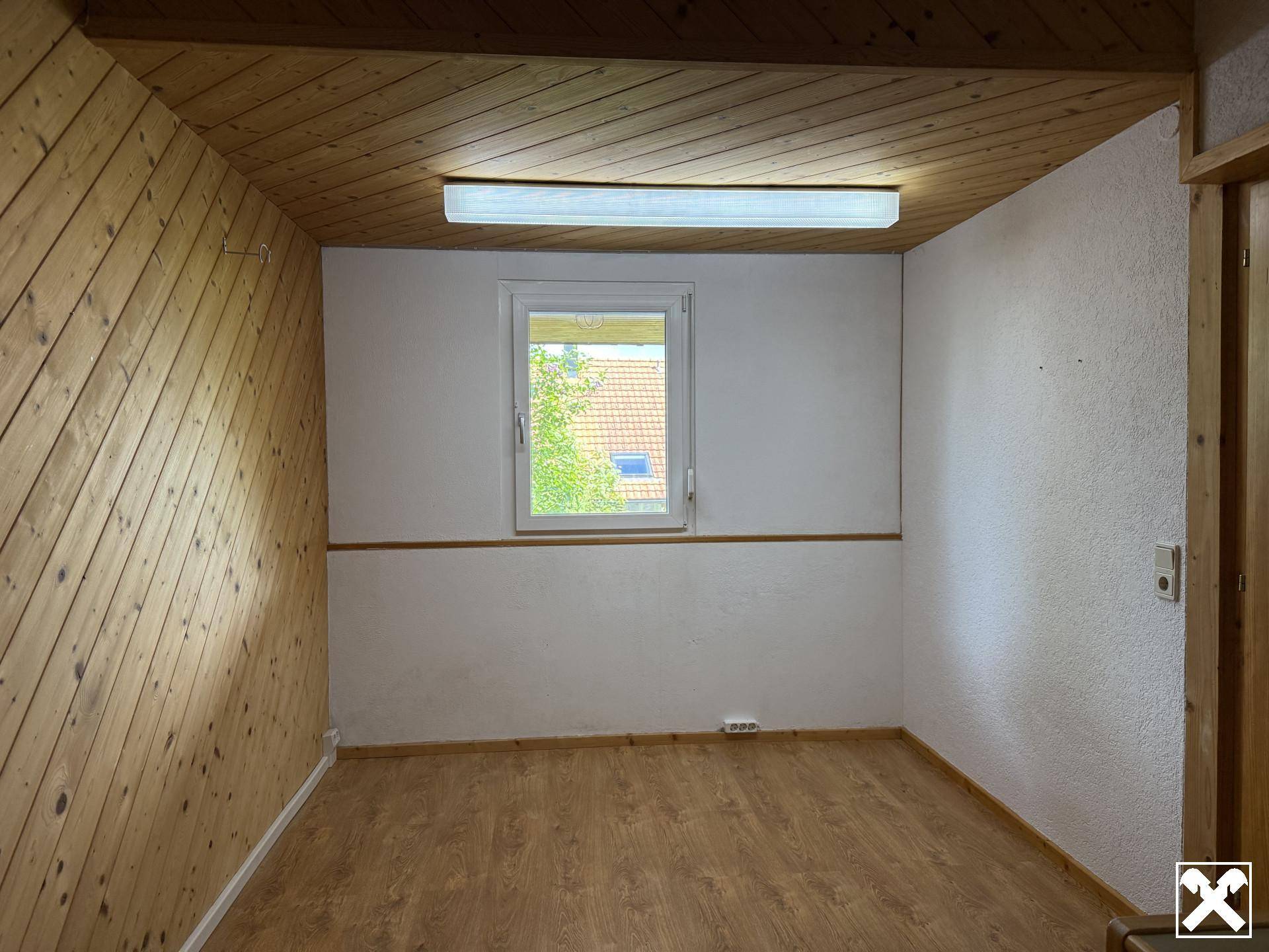 Leeres Zimmer mit Holzwänden und -decke, einem Fenster und Laminatboden, bereit zur individuellen Gestaltung.