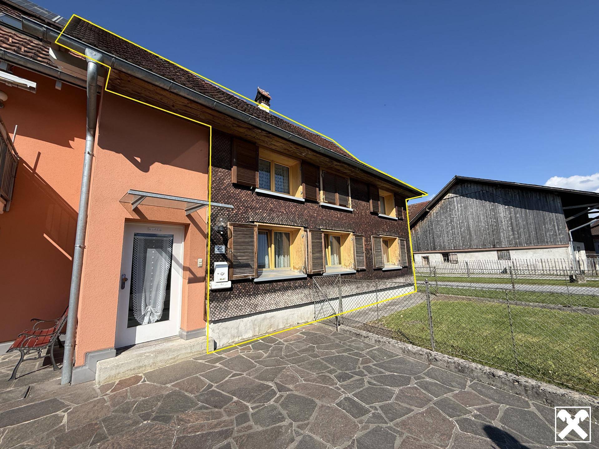 Eingangsbereich des Hauses mit orangefarbener Fassade, Holzverkleidung und gepflastertem Vorplatz.