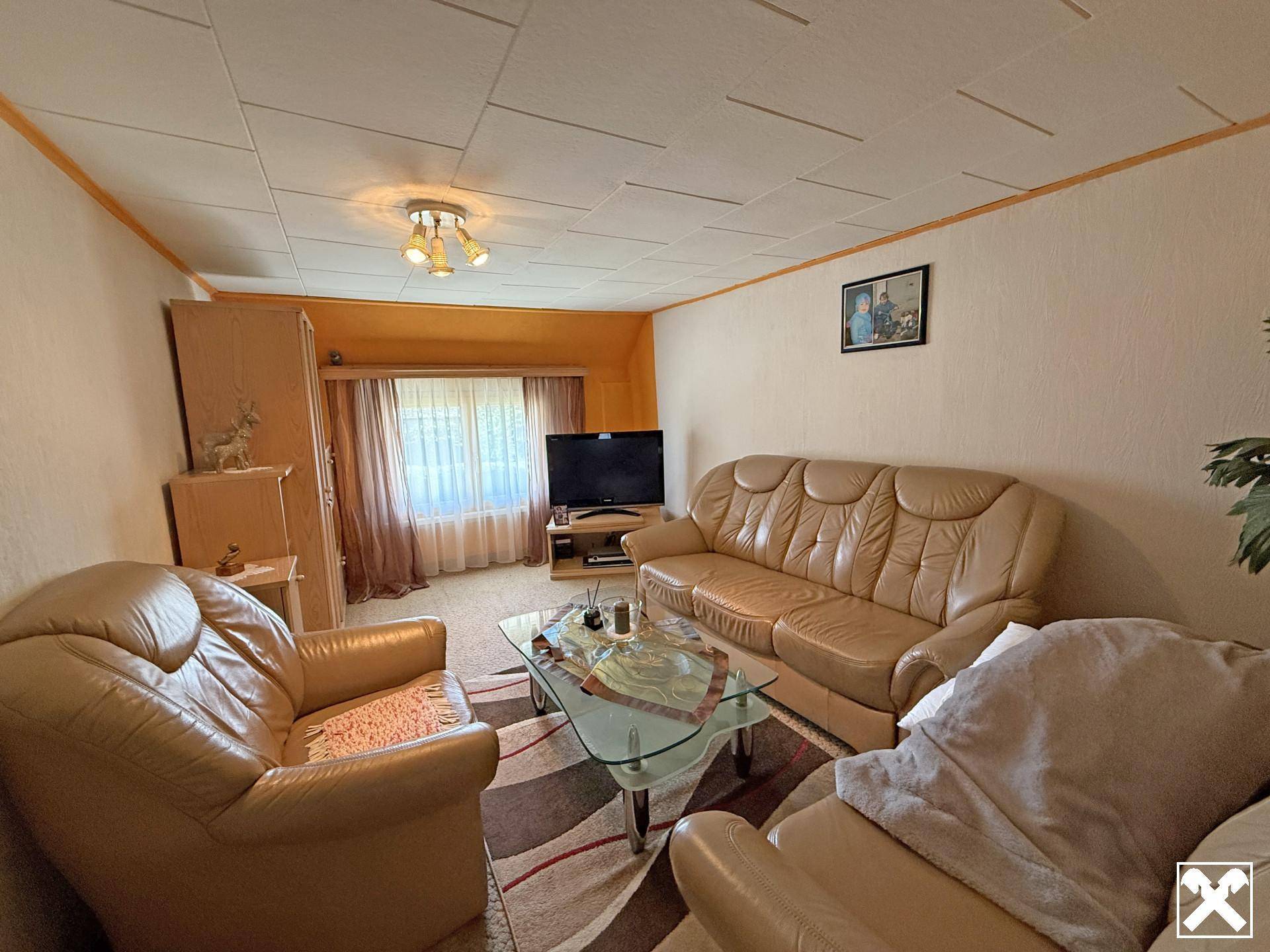 Gemütliches Wohnzimmer mit beigefarbenen Ledersofas, Glastisch und Fernseher in traditionellem Stil.
