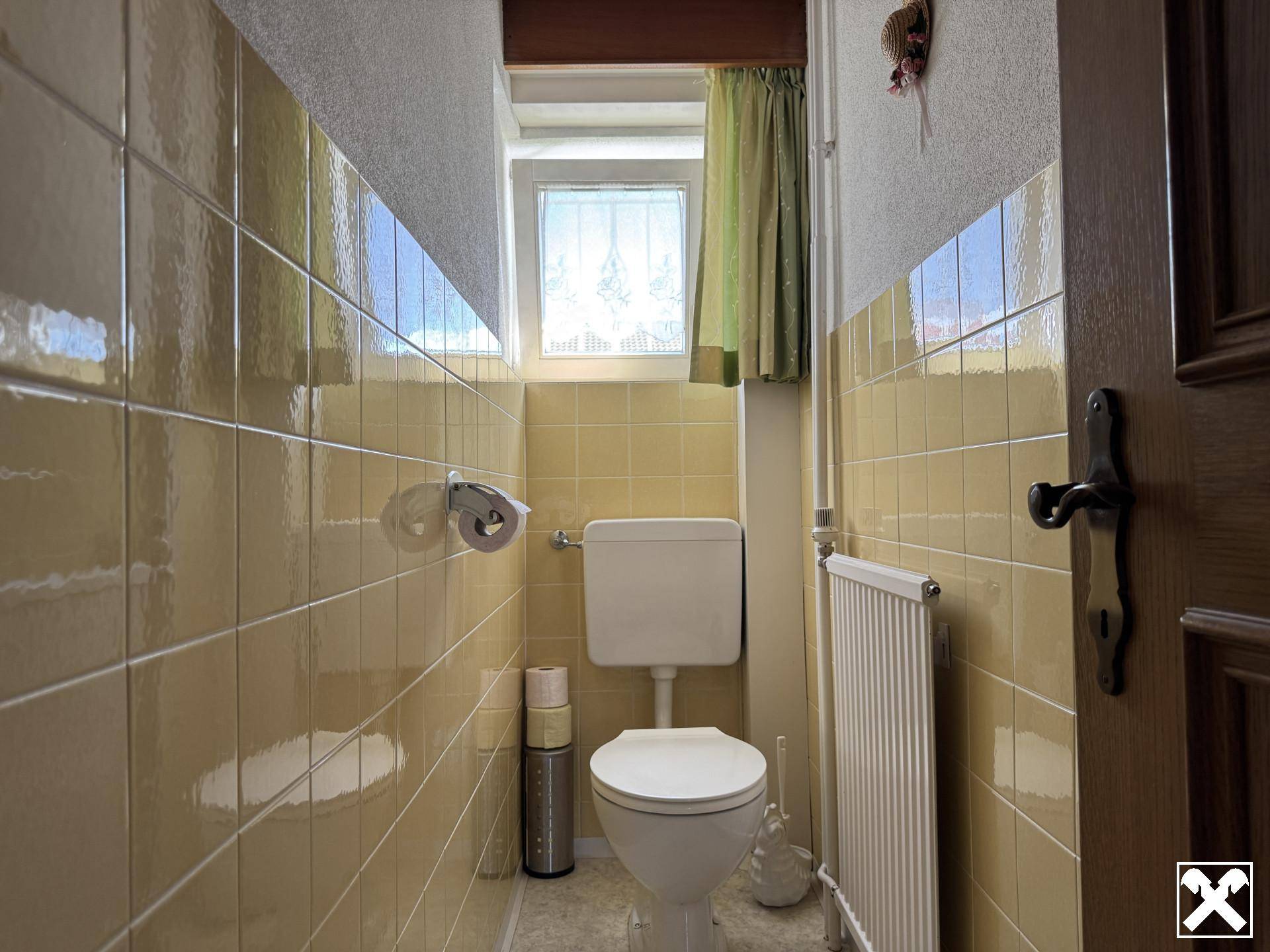 Separates WC mit gelben Fliesen, Toilette und kleinem Fenster für Belüftung.