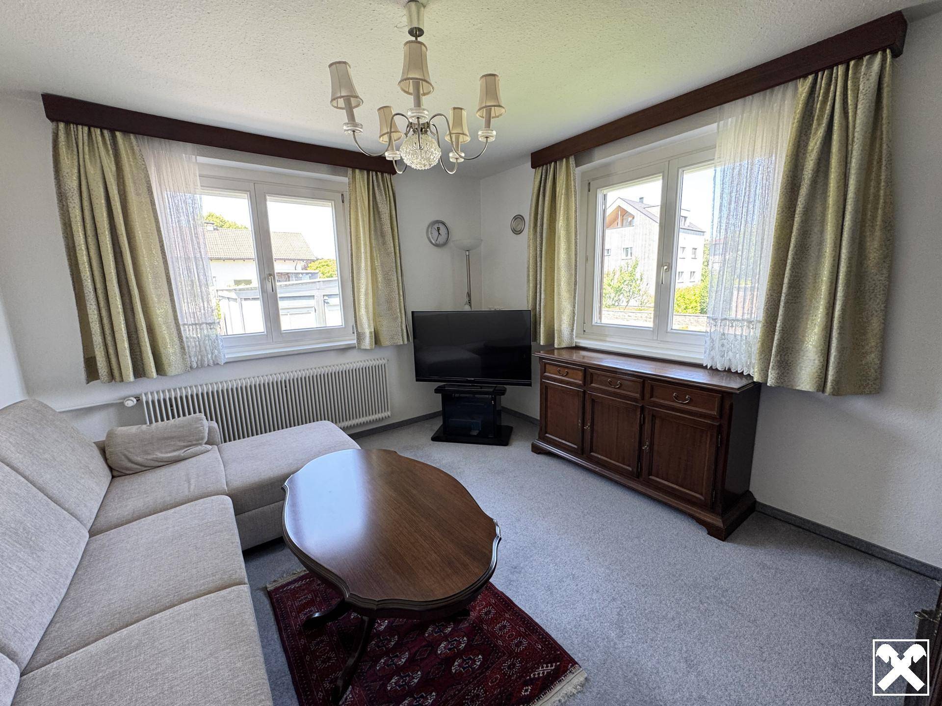 Wohnzimmer mit Teppichboden, beiger Couch und traditionellen Holzmöbeln.