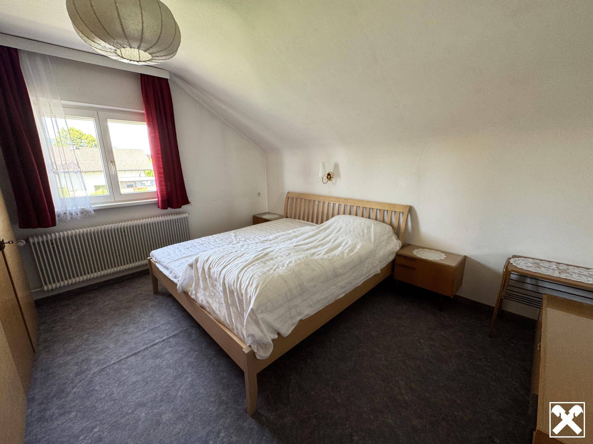 Schlafzimmer im Dachgeschoss mit schrägen Wänden, Doppelbett und Fenster.