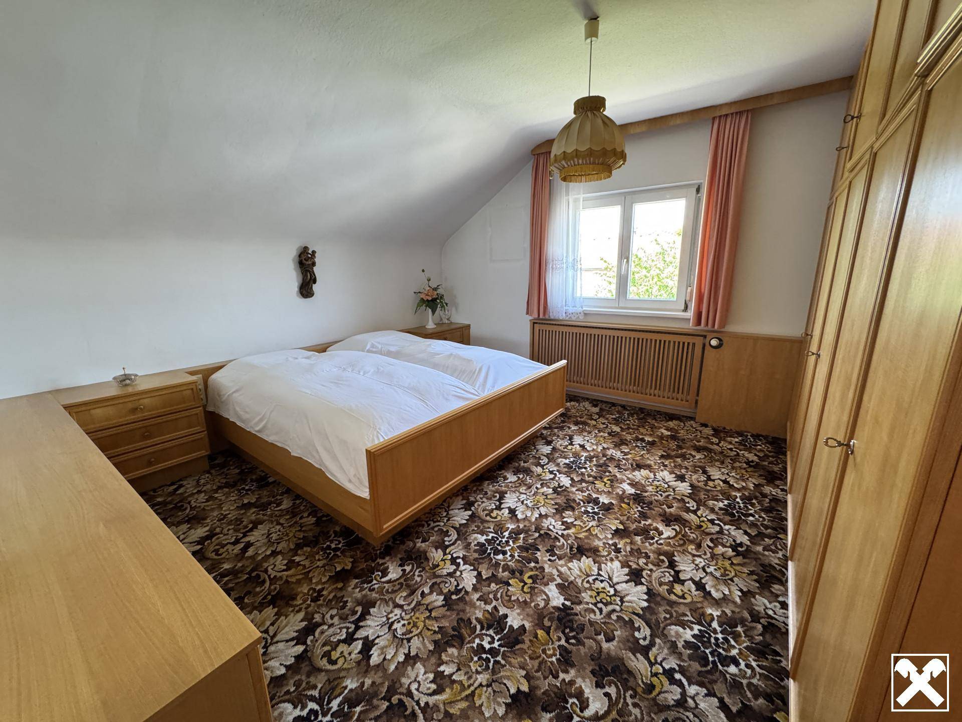 Geräumiges Schlafzimmer mit gemustertem Teppichboden, Holzmöbeln und Fenster.