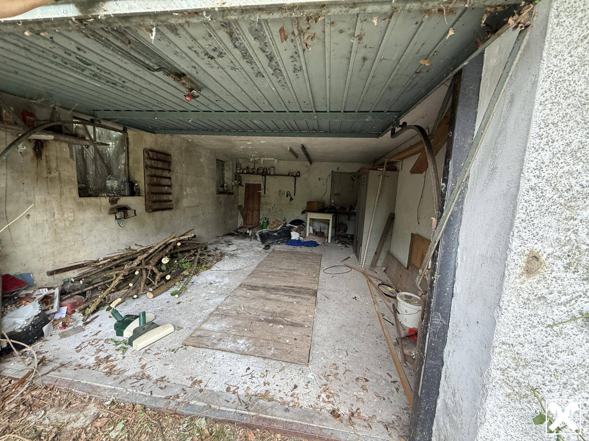 Unaufgeräumte und verfallene Garage oder Abstellraum mit Betonboden und Holzstapeln.