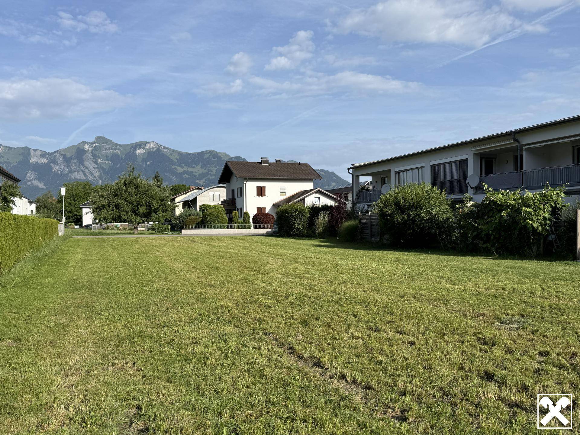 Ausgedehnte Rasenfläche eines Grundstücks mit angrenzenden Wohnhäusern und einer malerischen Bergkulisse.