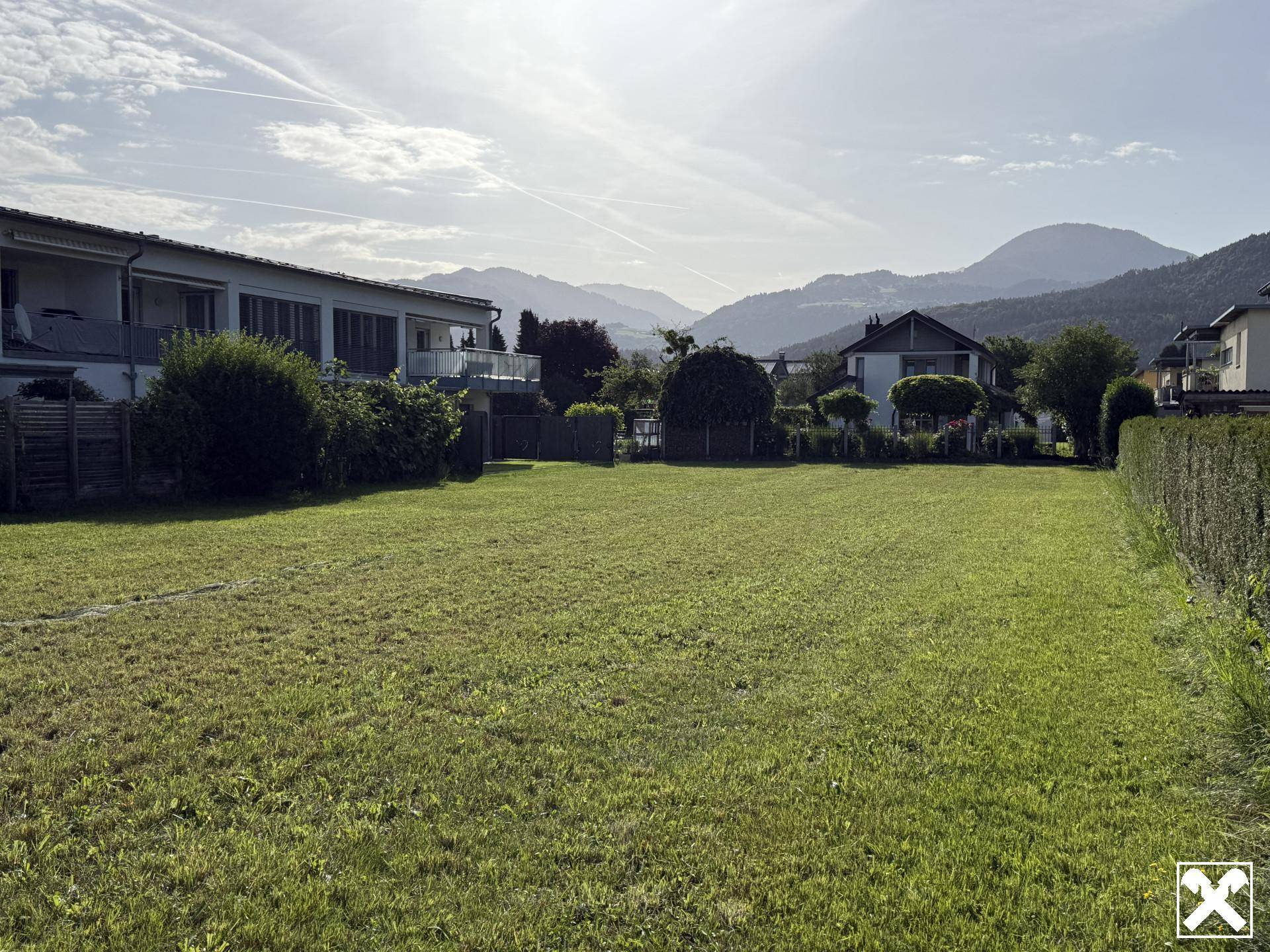 Große Rasenfläche eines Grundstücks mit umliegenden Häusern und einer beeindruckenden Berglandschaft im Hintergrund.