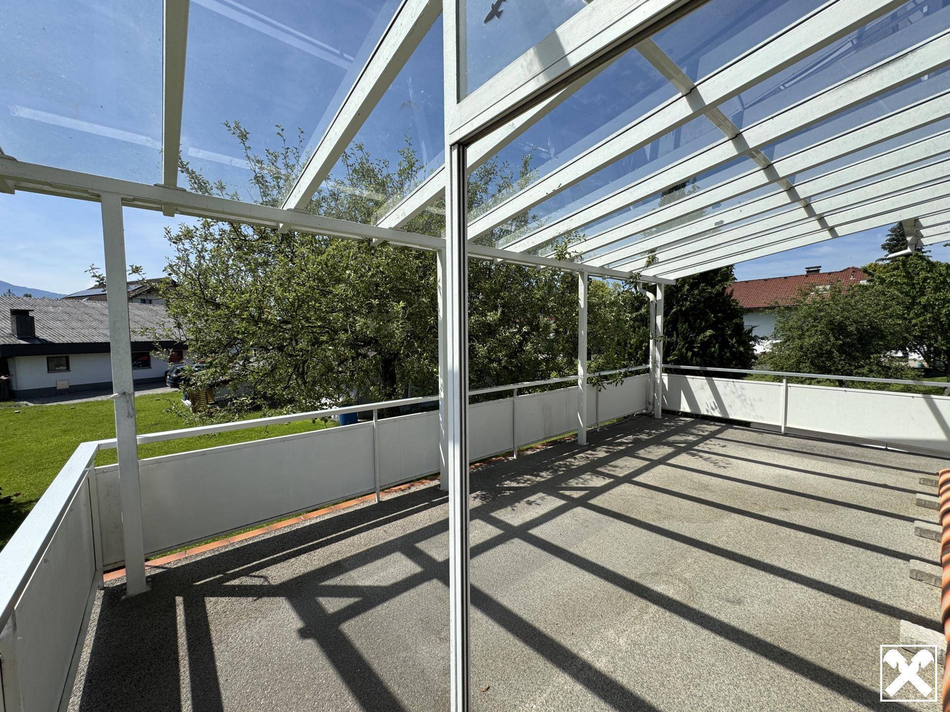Überdachter Balkon mit Glasdach und Metallgeländer, bietet einen geschützten Außenbereich.