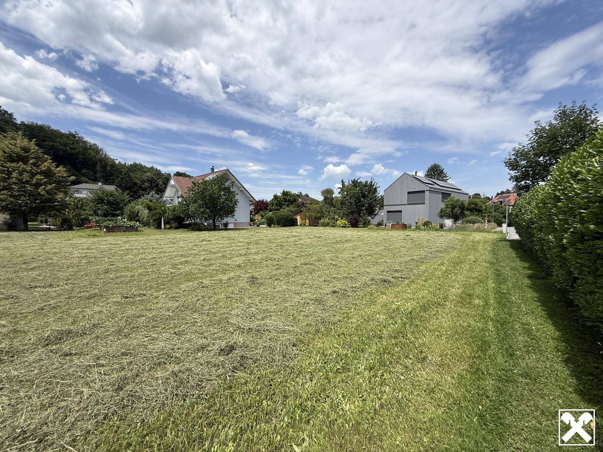 Weitläufige, gepflegte Rasenfläche mit angrenzenden Wohnhäusern und einer grünen Hecke unter blauem Himmel.