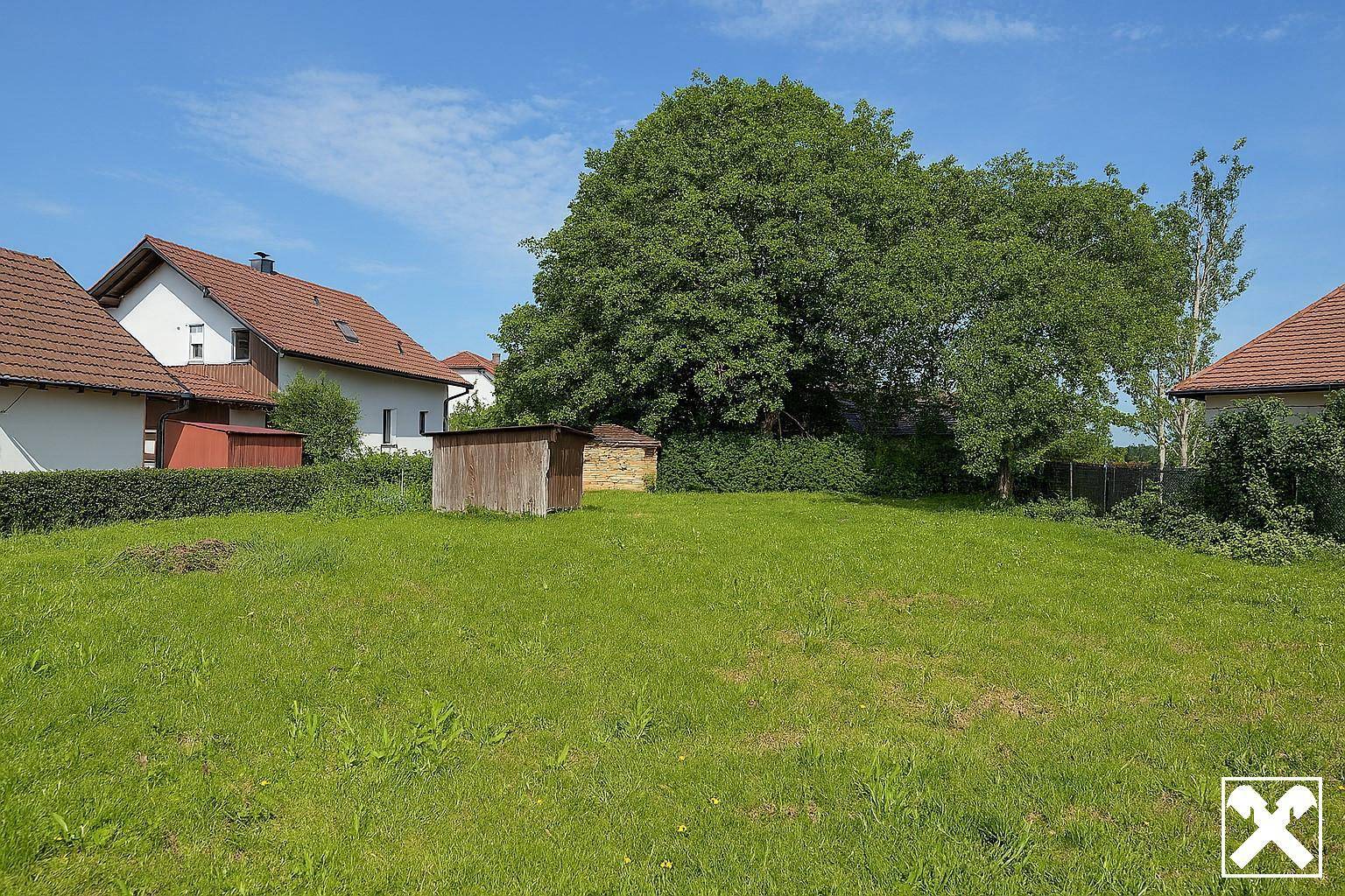 Weitläufige Rasenfläche mit einem Holzschuppen, umgeben von Bäumen und Wohnhäusern.