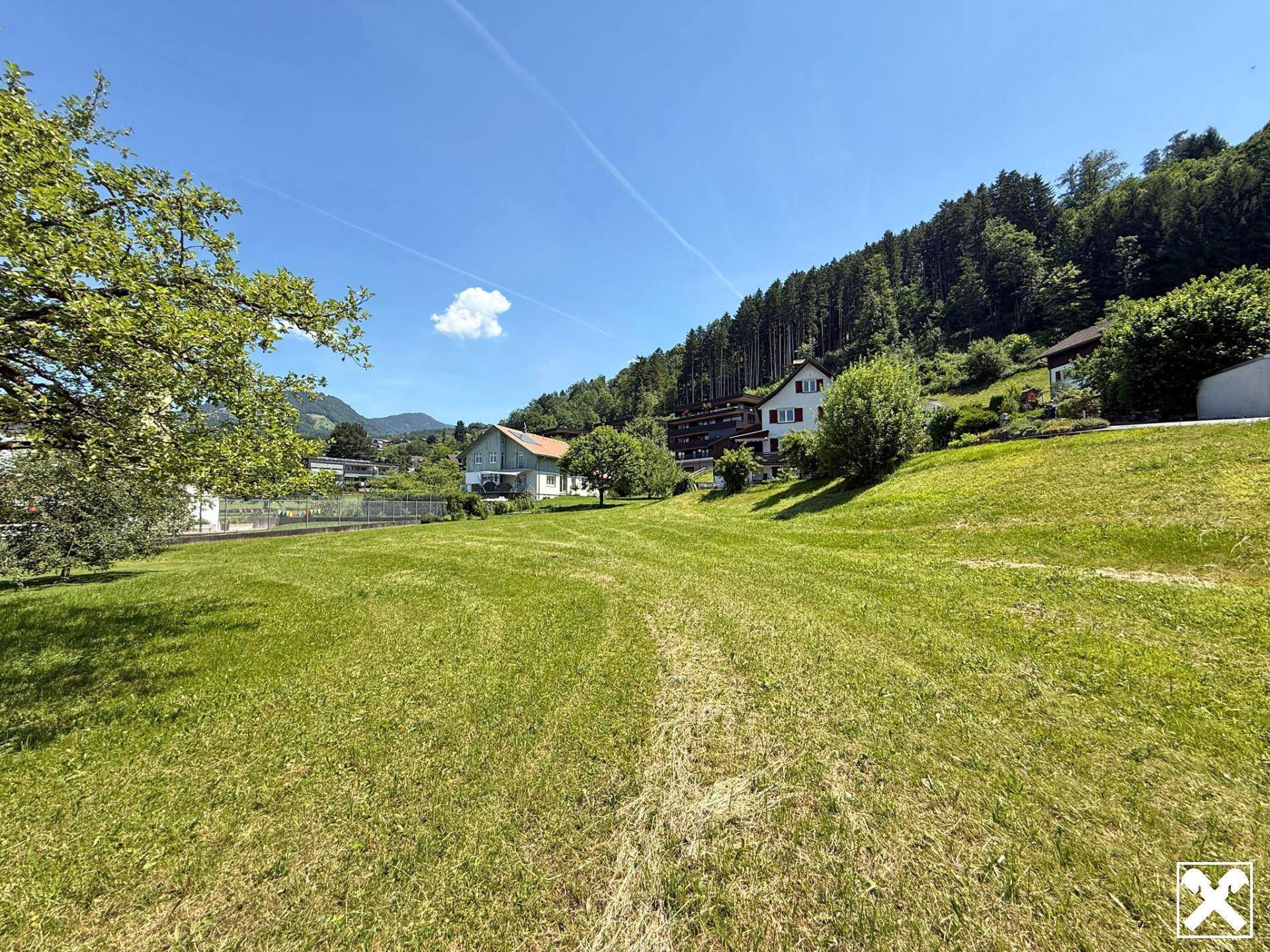 Idyllische grüne Landschaft mit weitem Blick auf bewaldete Hügel und umliegende Häuser.