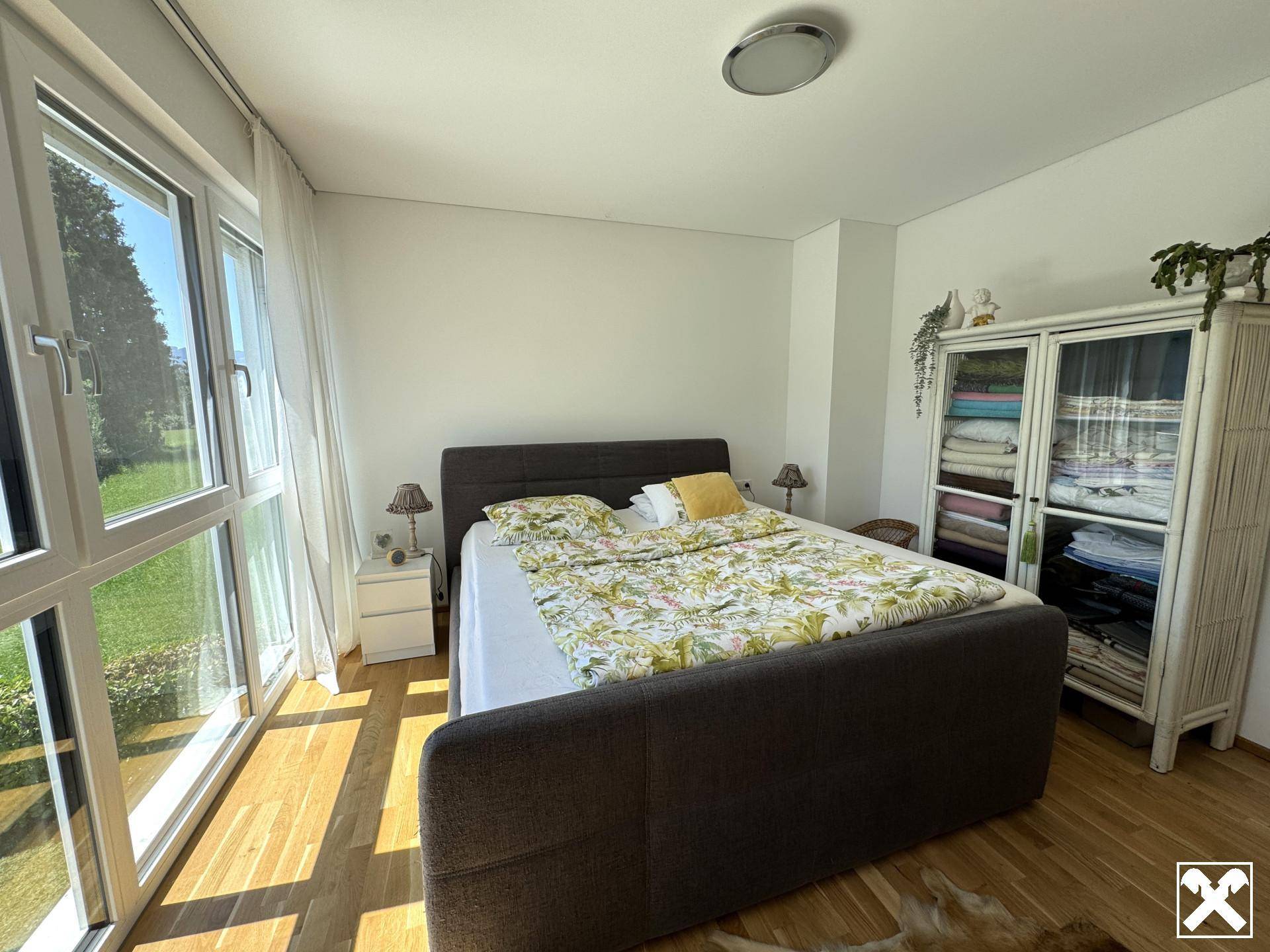 Helles Schlafzimmer mit großzügigen Fenstern, Doppelbett und Parkettboden, bietet viel Tageslicht.