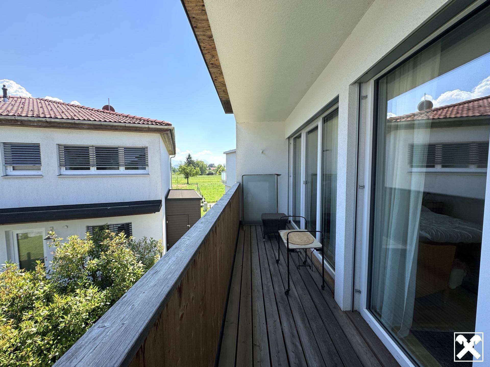 Langer Balkon mit Holzbelag und Sitzgelegenheiten, bietet einen Blick ins Grüne und auf die Umgebung.