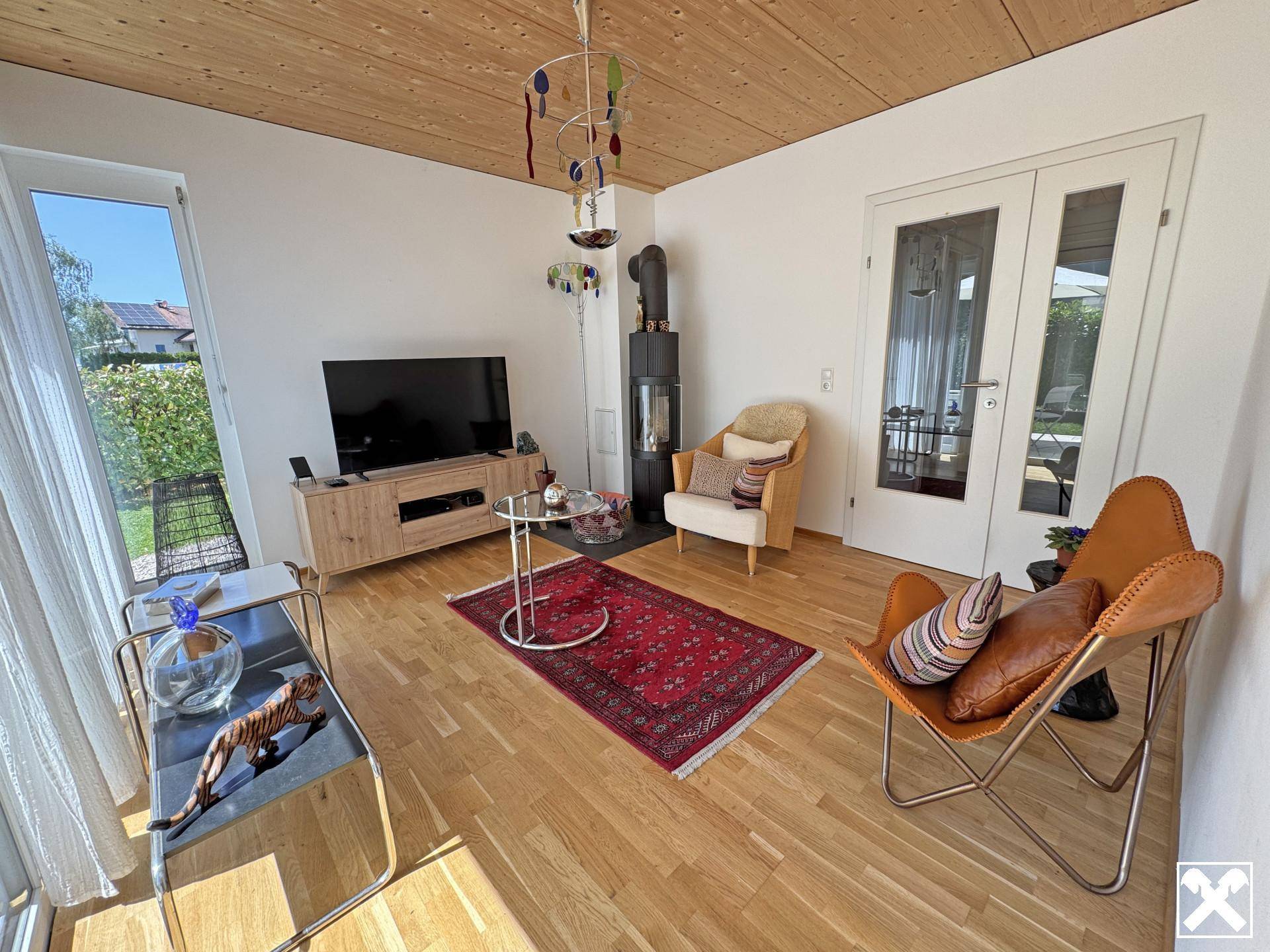 Helles Wohnzimmer mit modernem Holzofen, Parkettboden und großen Fenstern zum Garten.