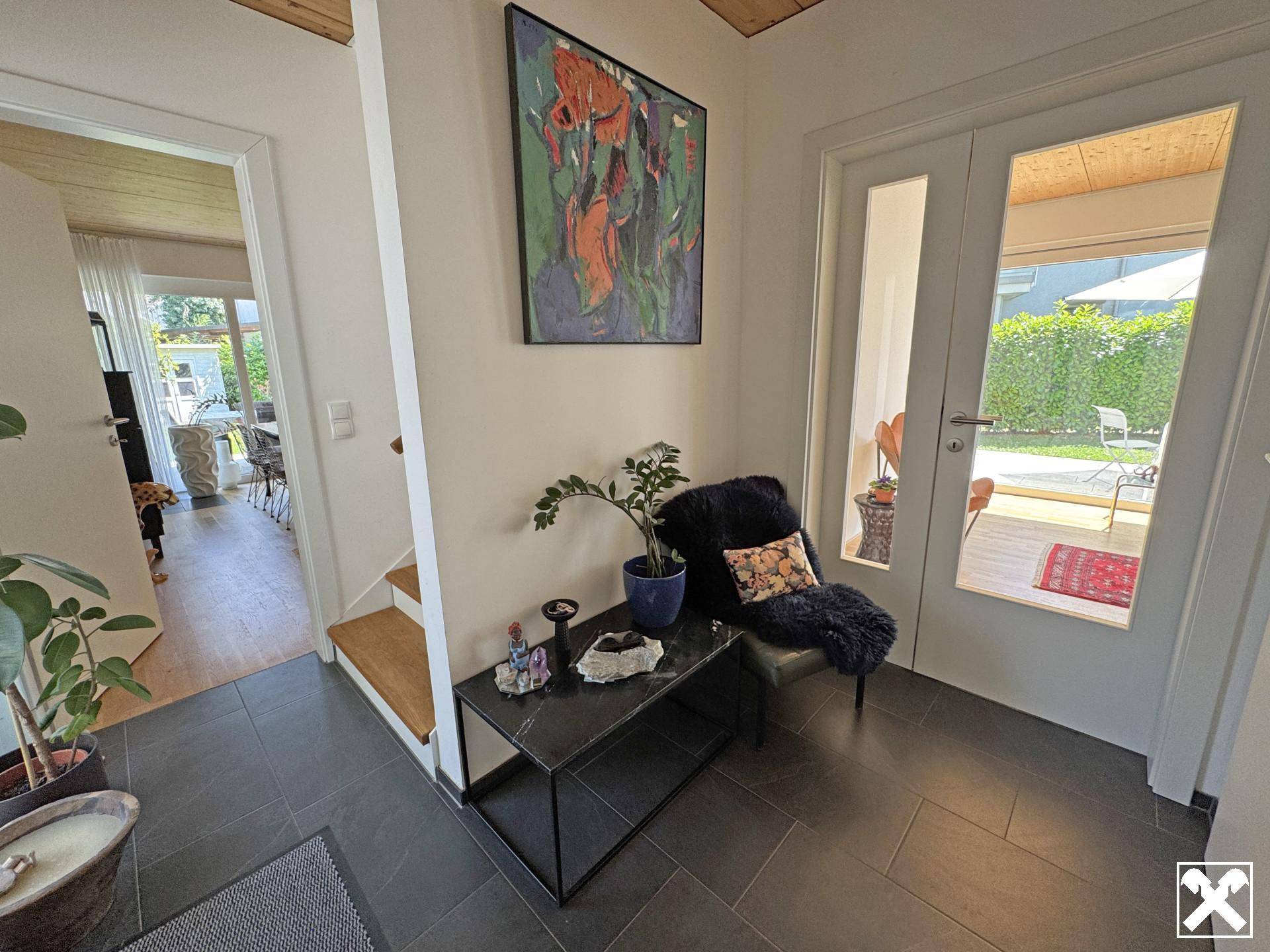 Heller Eingangsbereich mit dunklen Fliesen, Kunstwerk und direktem Zugang zur Terrasse und zum Garten.