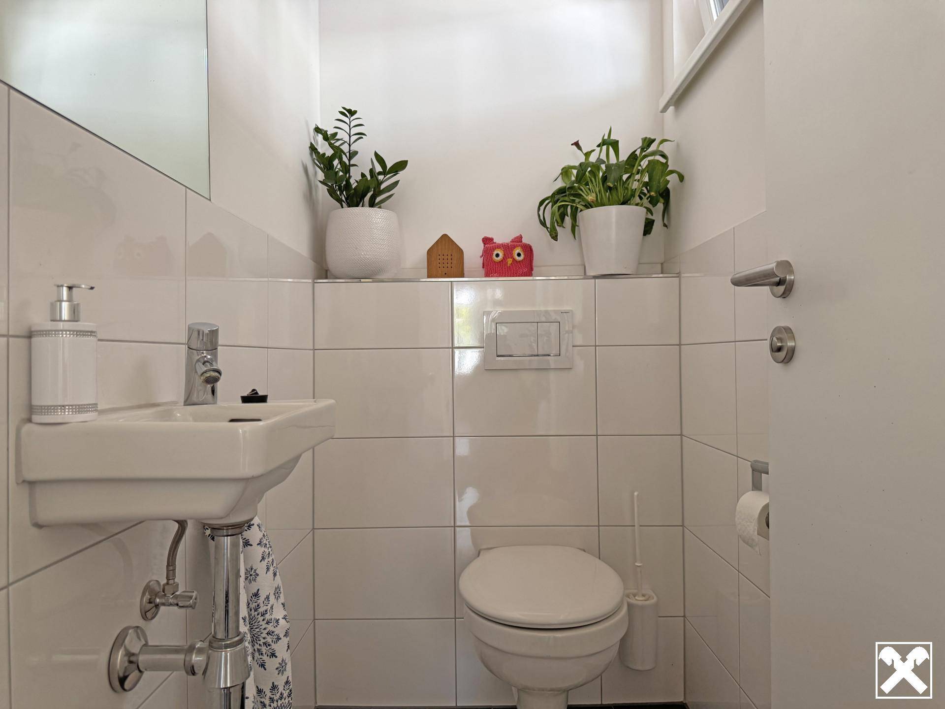 Kleines Gäste-WC mit Waschbecken und Toilette, hell gefliest und funktional eingerichtet.