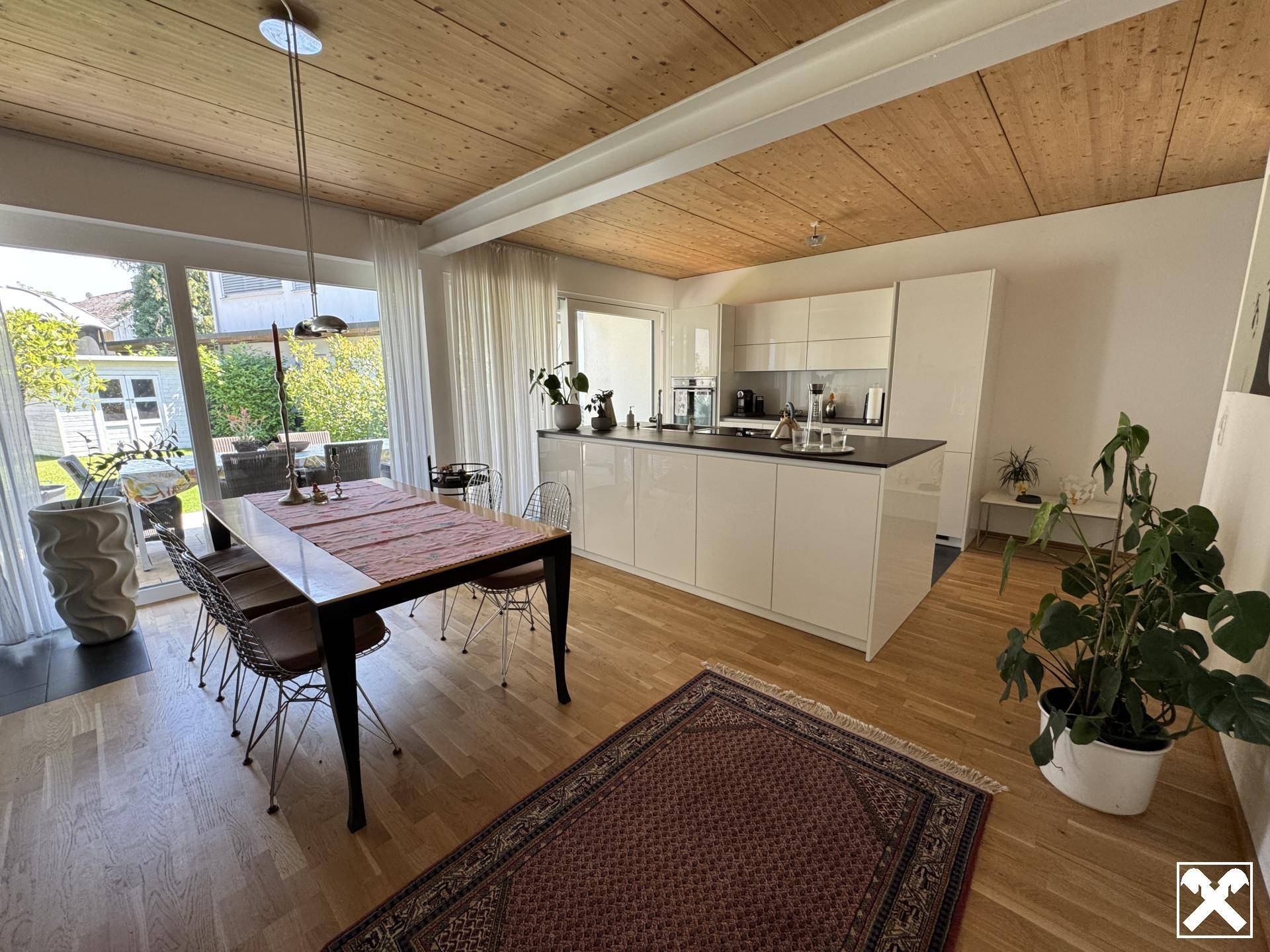 Heller offener Wohn-Essbereich mit moderner Küche, Holzbalkendecke und Zugang zum Garten.