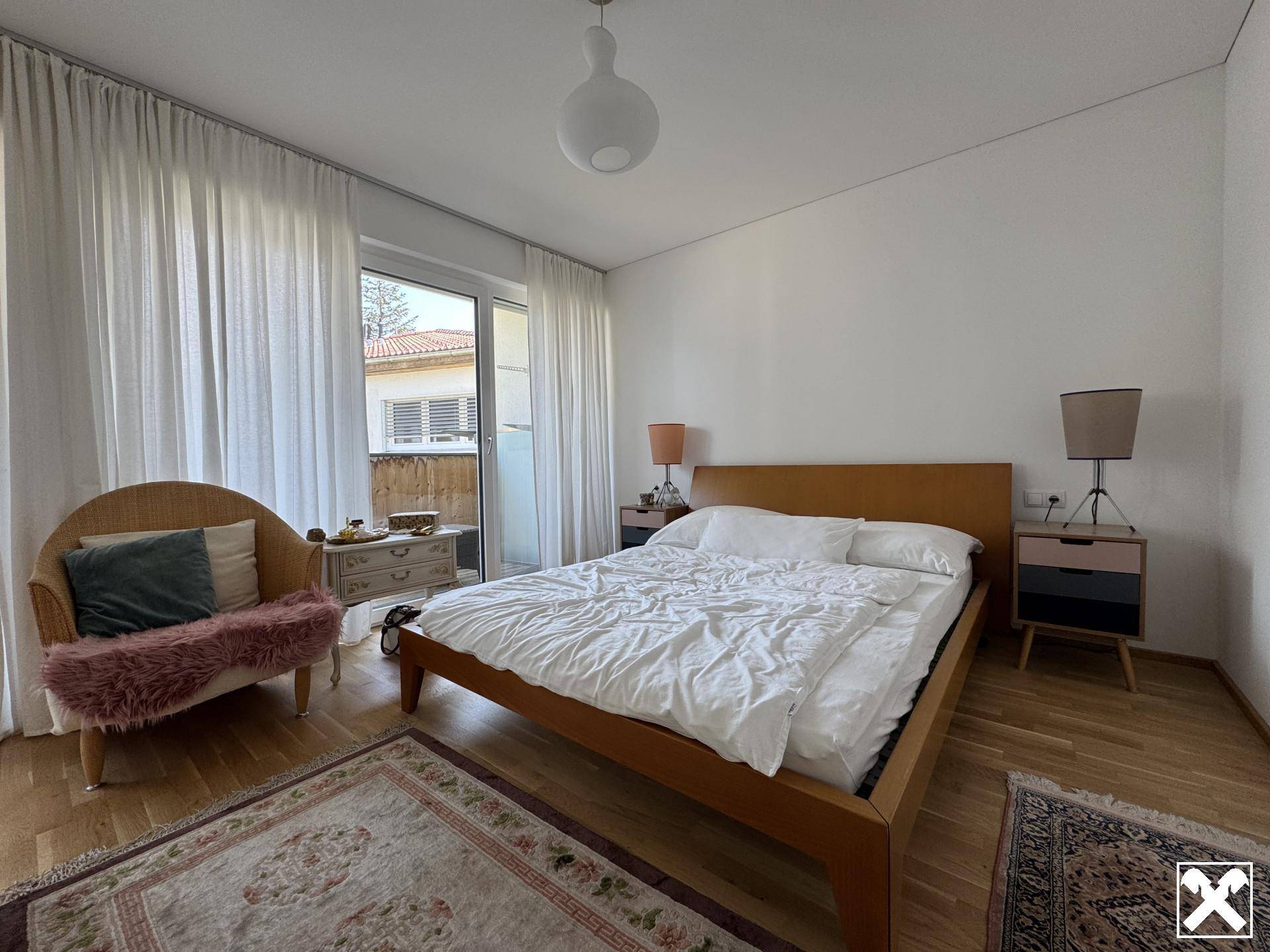 Schlafzimmer mit Doppelbett, Holzboden und Zugang zu einem kleinen Balkon, hell und freundlich.