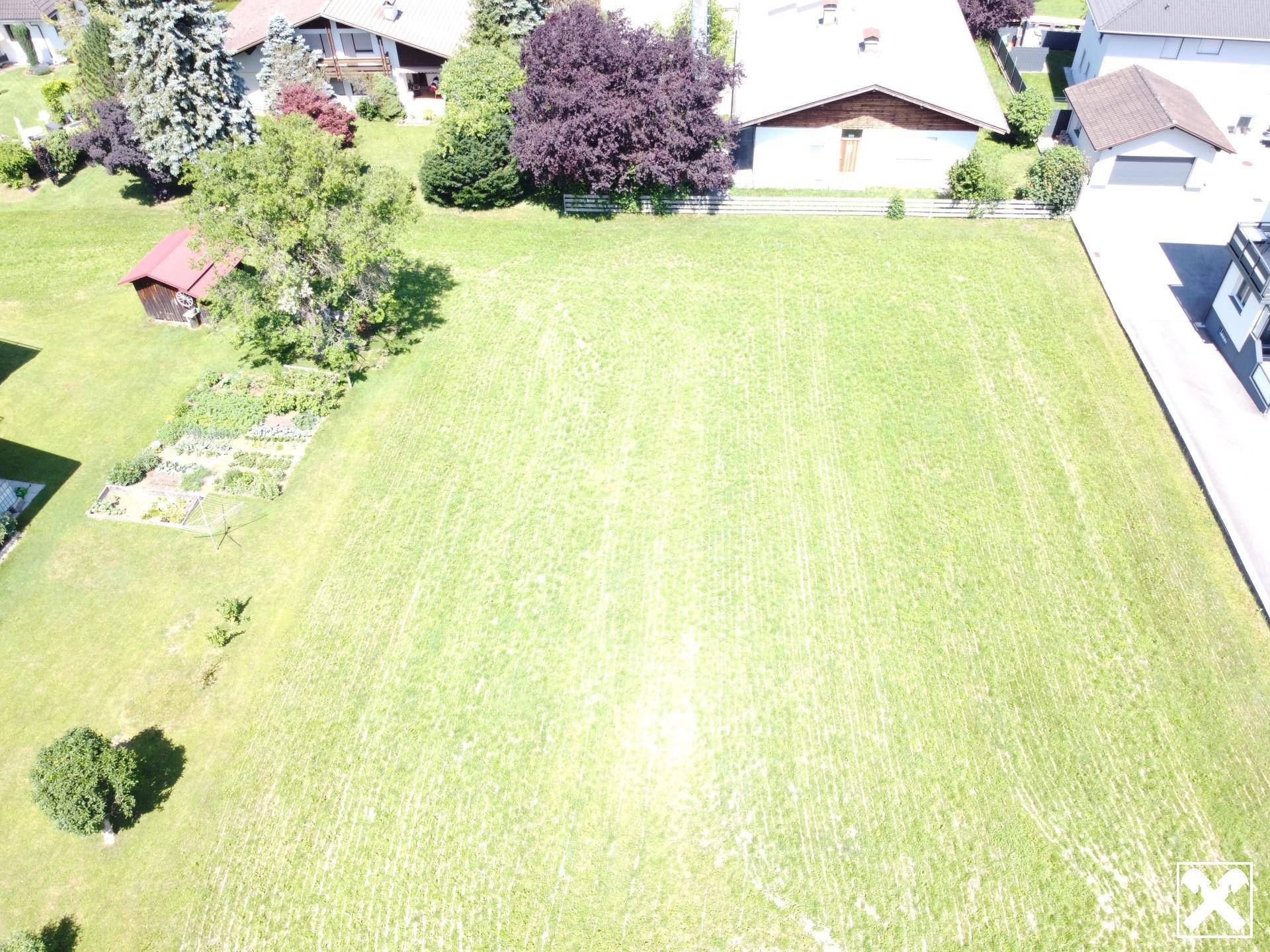 Luftaufnahme eines großen grünen Grundstücks mit angrenzendem Gemüsegarten und umliegenden Häusern.