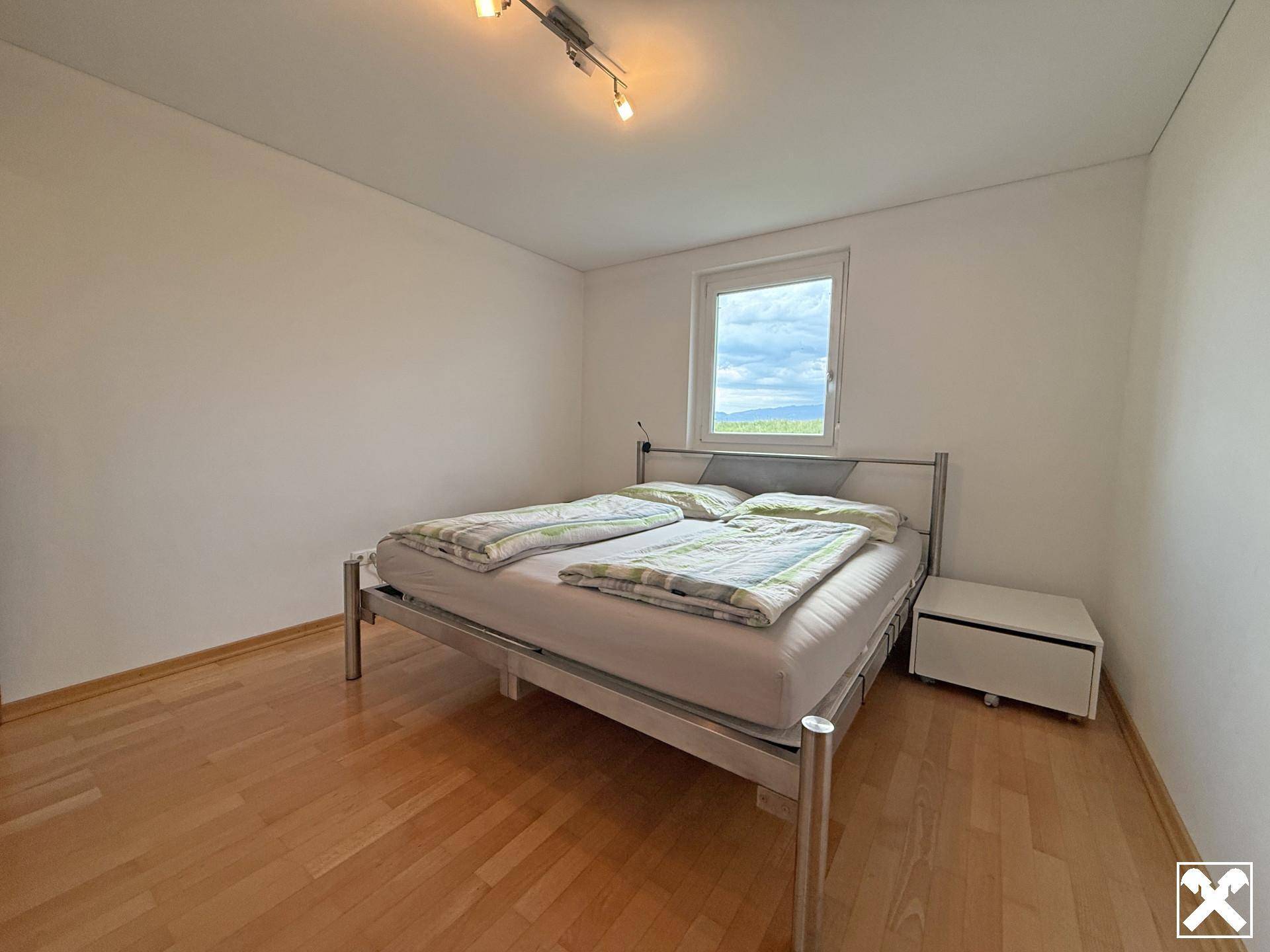 Helles Schlafzimmer mit Holzboden, Doppelbett und Fenster mit Blick ins Grüne.