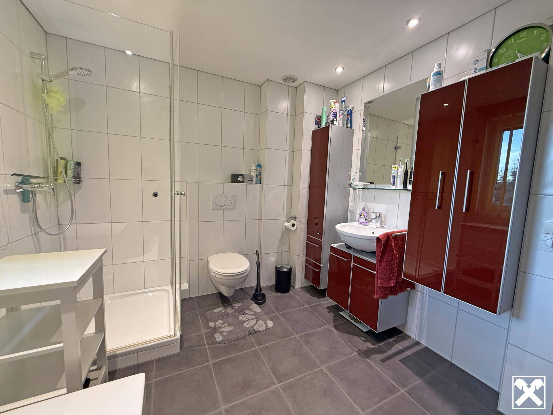 Modernes Badezimmer mit Duschkabine, Waschtisch, WC und roten Schränken für Stauraum.