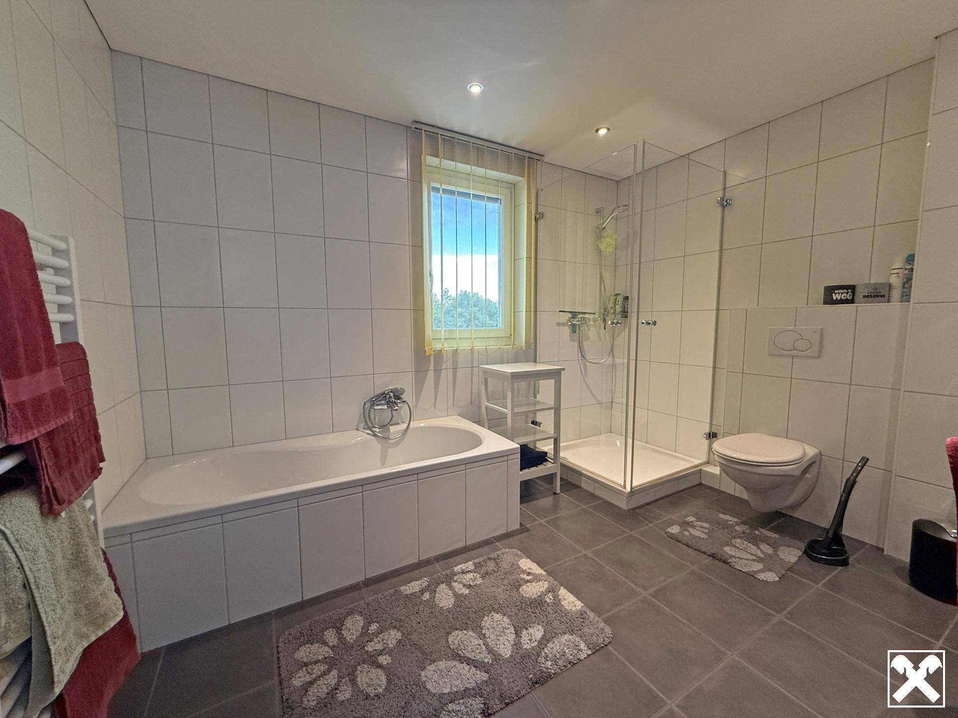 Geräumiges Badezimmer mit Badewanne, Duschkabine, WC und Fenster für Tageslicht.