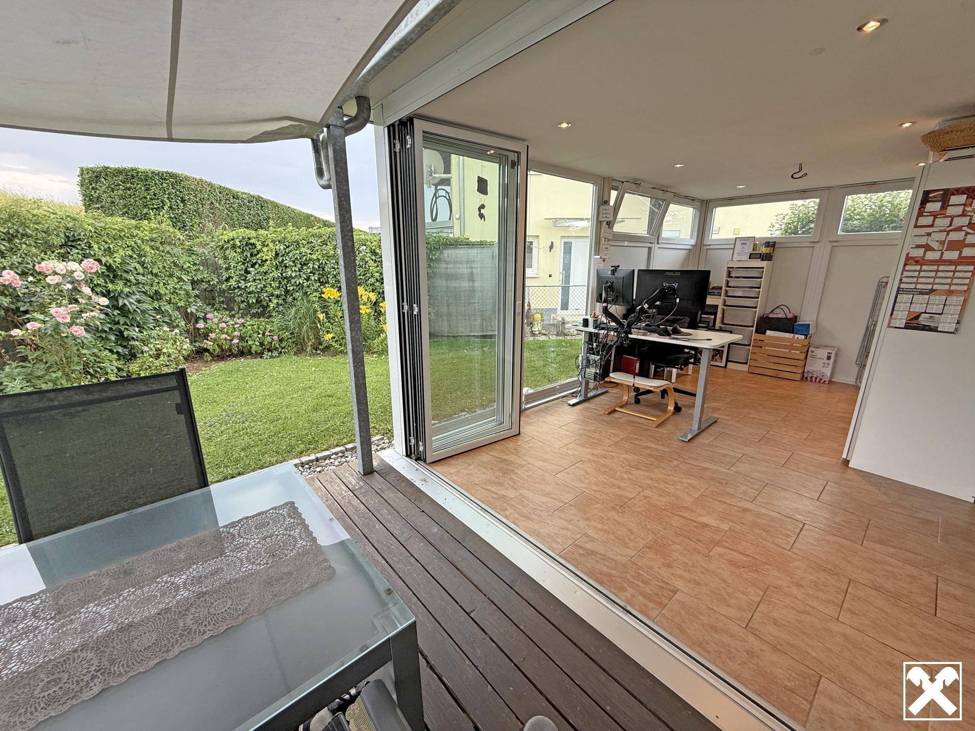 Heller Wintergarten mit großen Glasfronten, Holzboden und Blick auf den gepflegten Garten.