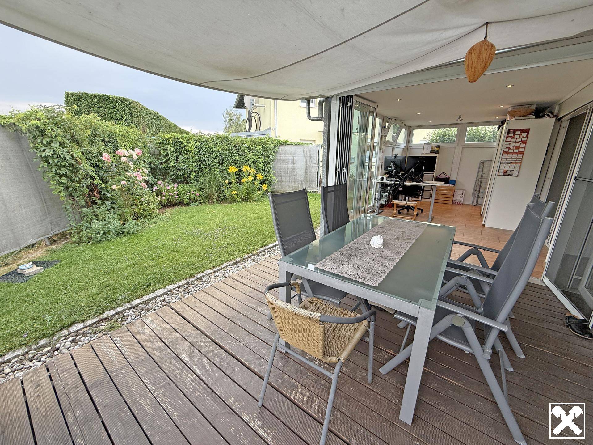 Gemütliche Holzterrasse mit Gartenmöbeln und Blick auf den grünen, blühenden Gartenbereich.