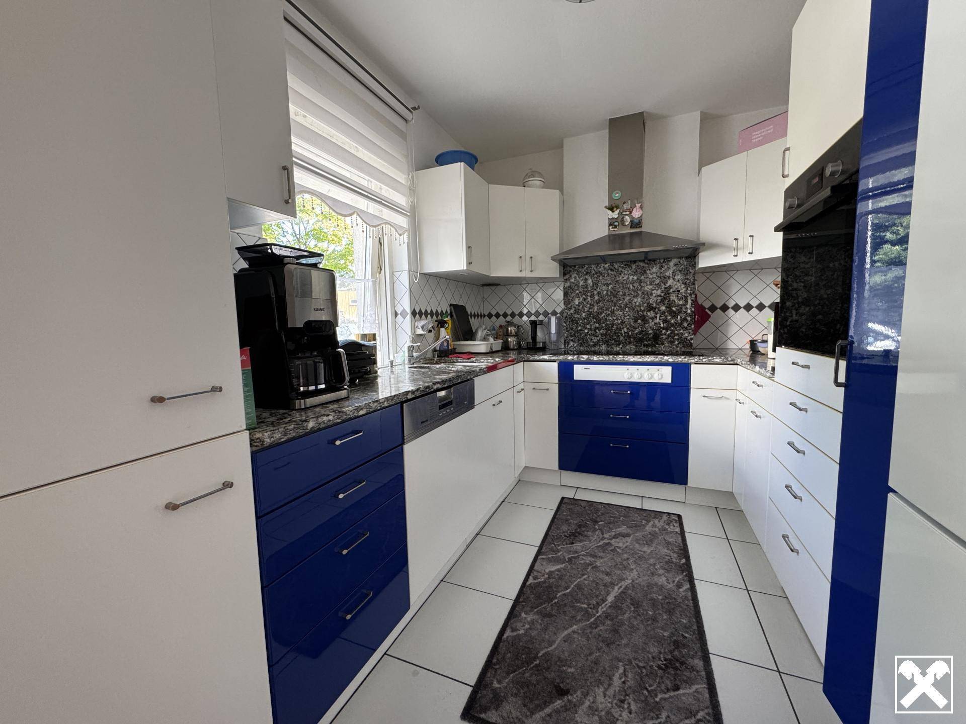 Moderne Küche mit blauen und weißen Schränken, Granitarbeitsplatten und Fliesenboden.