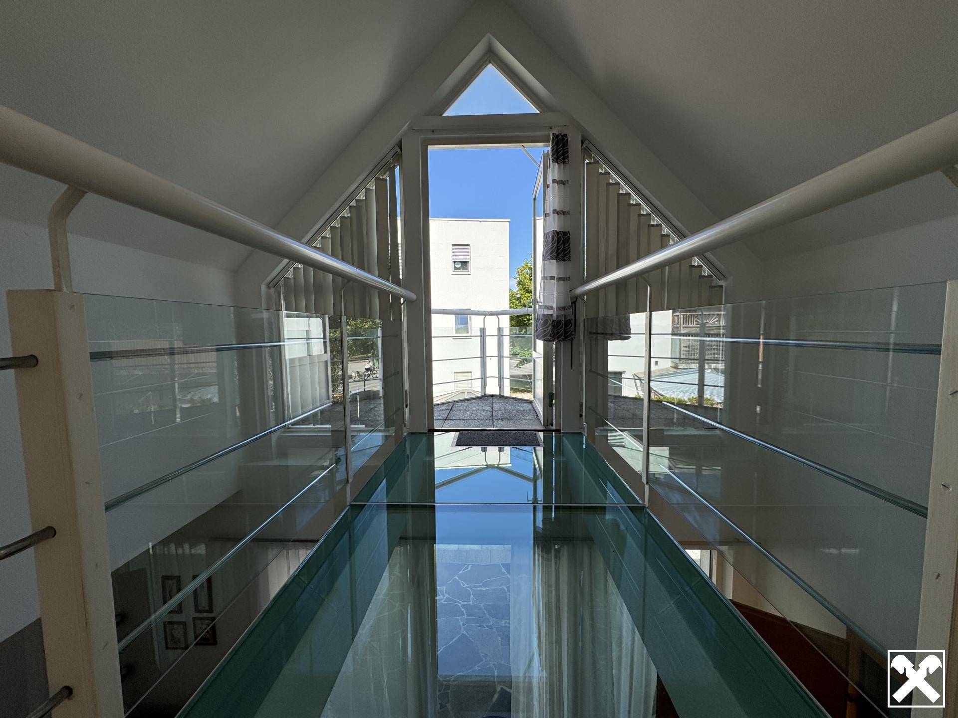 Heller Flur mit Glasbrücke und hohen Decken, der viel Tageslicht hereinlässt.