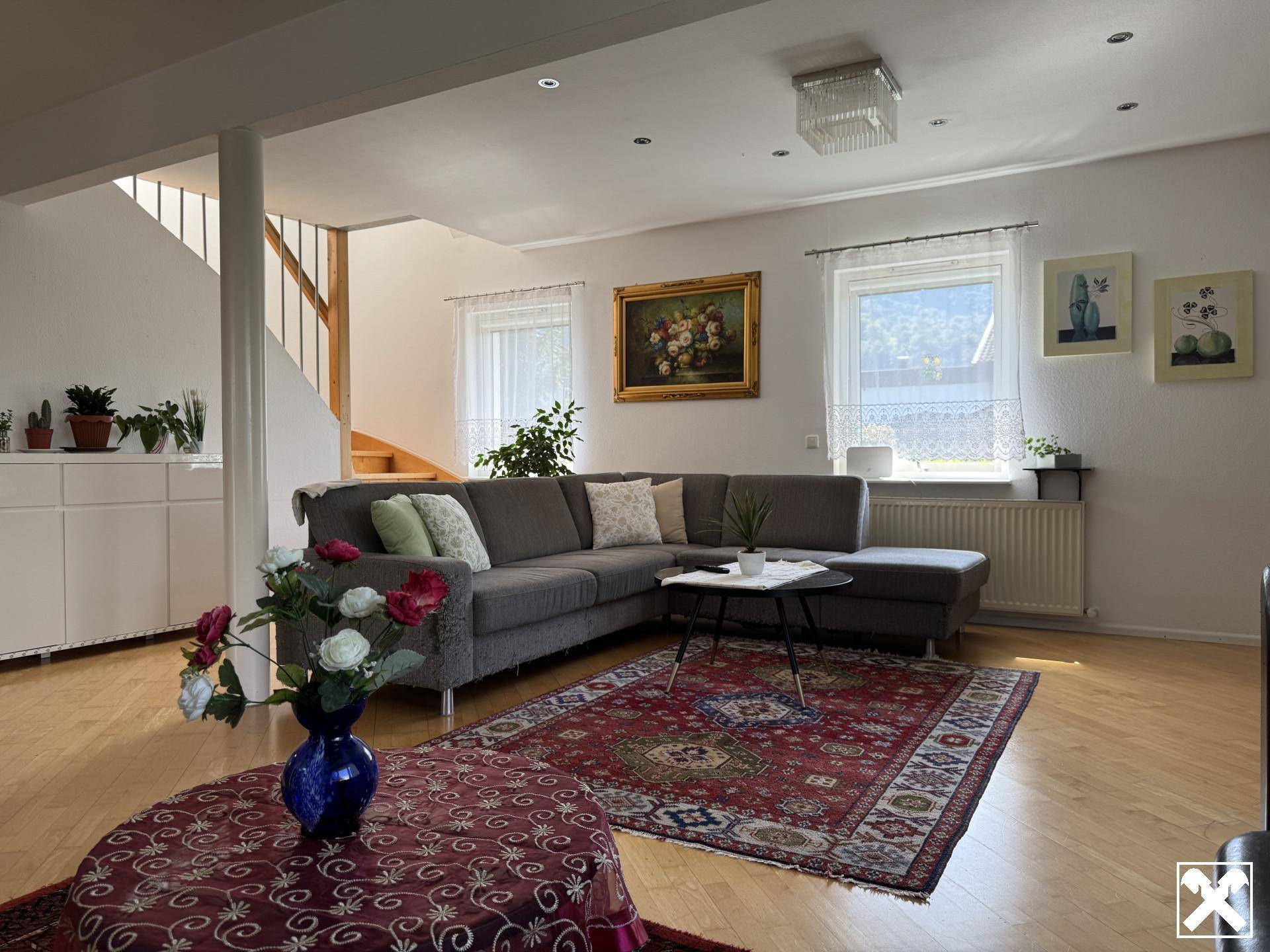 Geräumiges Wohnzimmer mit bequemer Couch, Holzboden und Zugang zu einer Treppe.