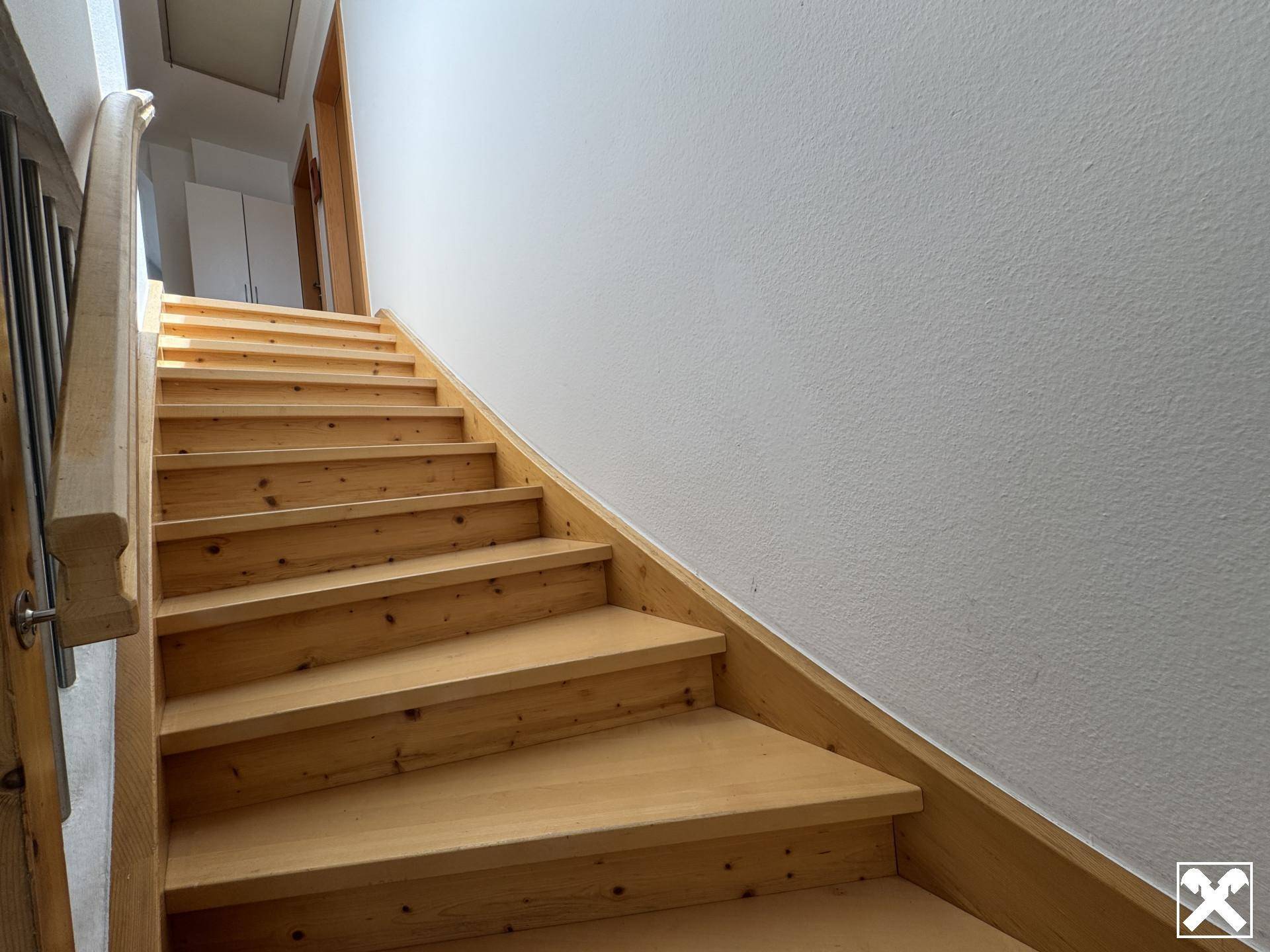 Helle Holztreppe führt in die oberen Stockwerke, umgeben von weißen Wänden.