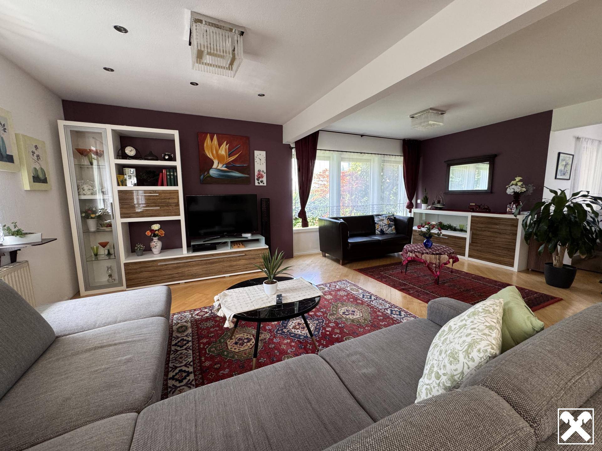 Geräumiges Wohnzimmer mit dunklen Akzentwänden, Holzboden und bequemen Sofas, ideal zum Entspannen.