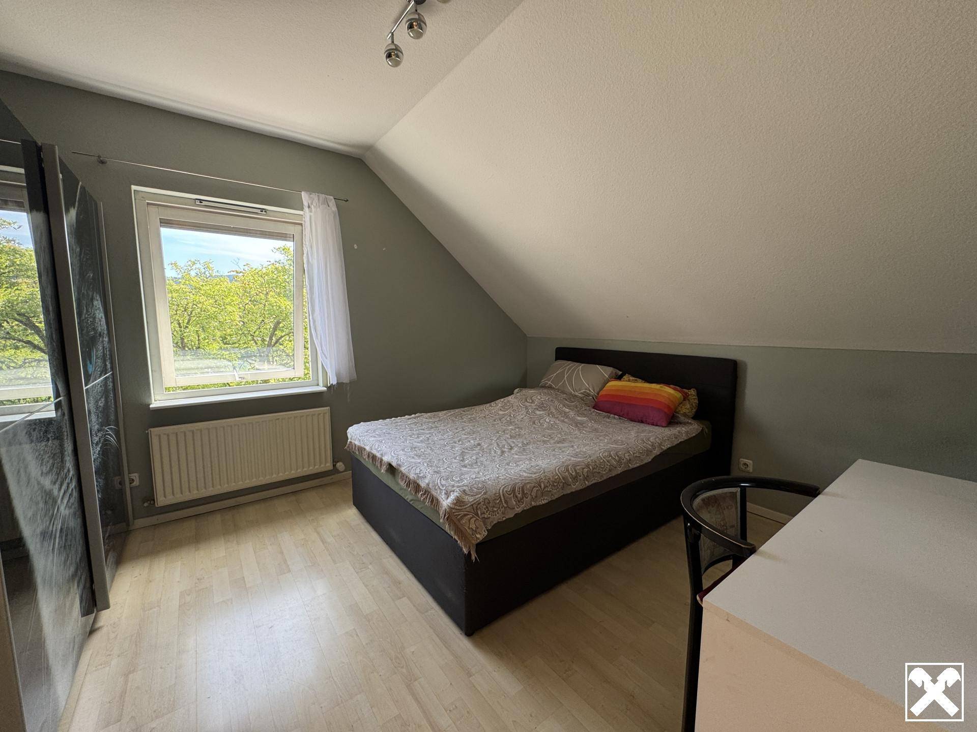 Helles Schlafzimmer im Dachgeschoss mit schräger Decke, Holzboden und Blick ins Grüne.