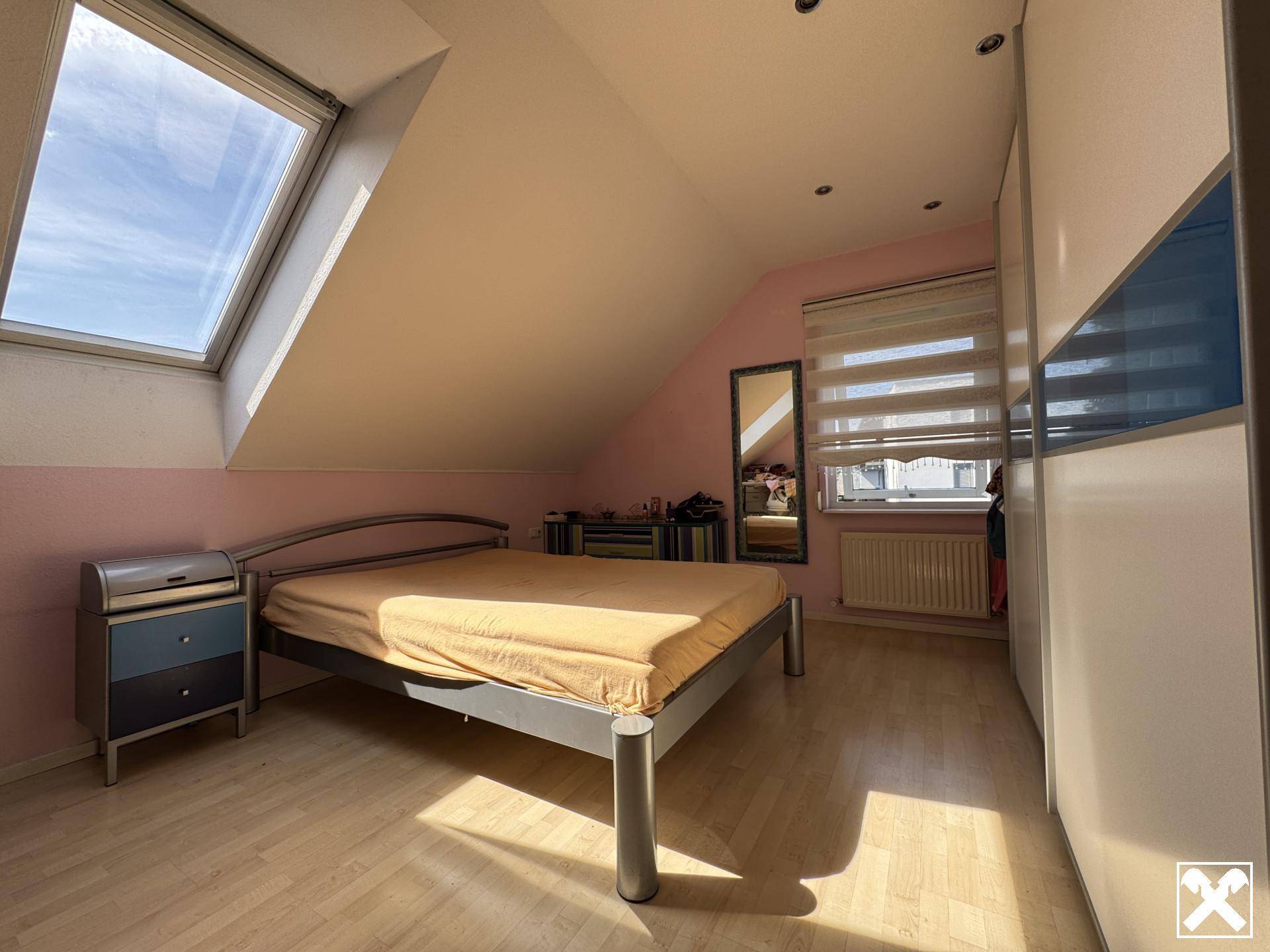 Gemütliches Schlafzimmer im Dachgeschoss mit großem Dachfenster, Holzboden und Kleiderschrank.