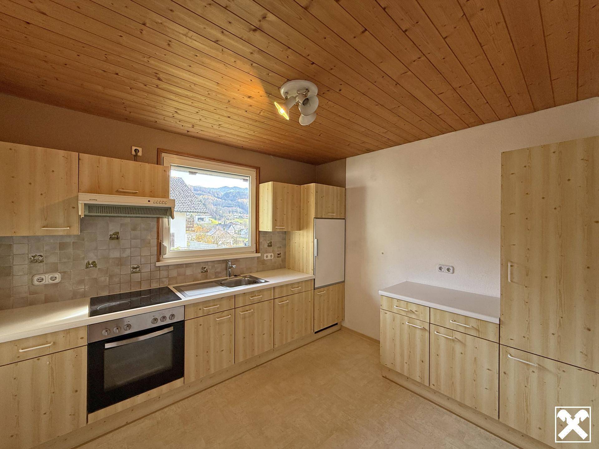 Helle Küche mit Holzschränken, Holzdecke und einem Fenster mit Blick auf die Umgebung.