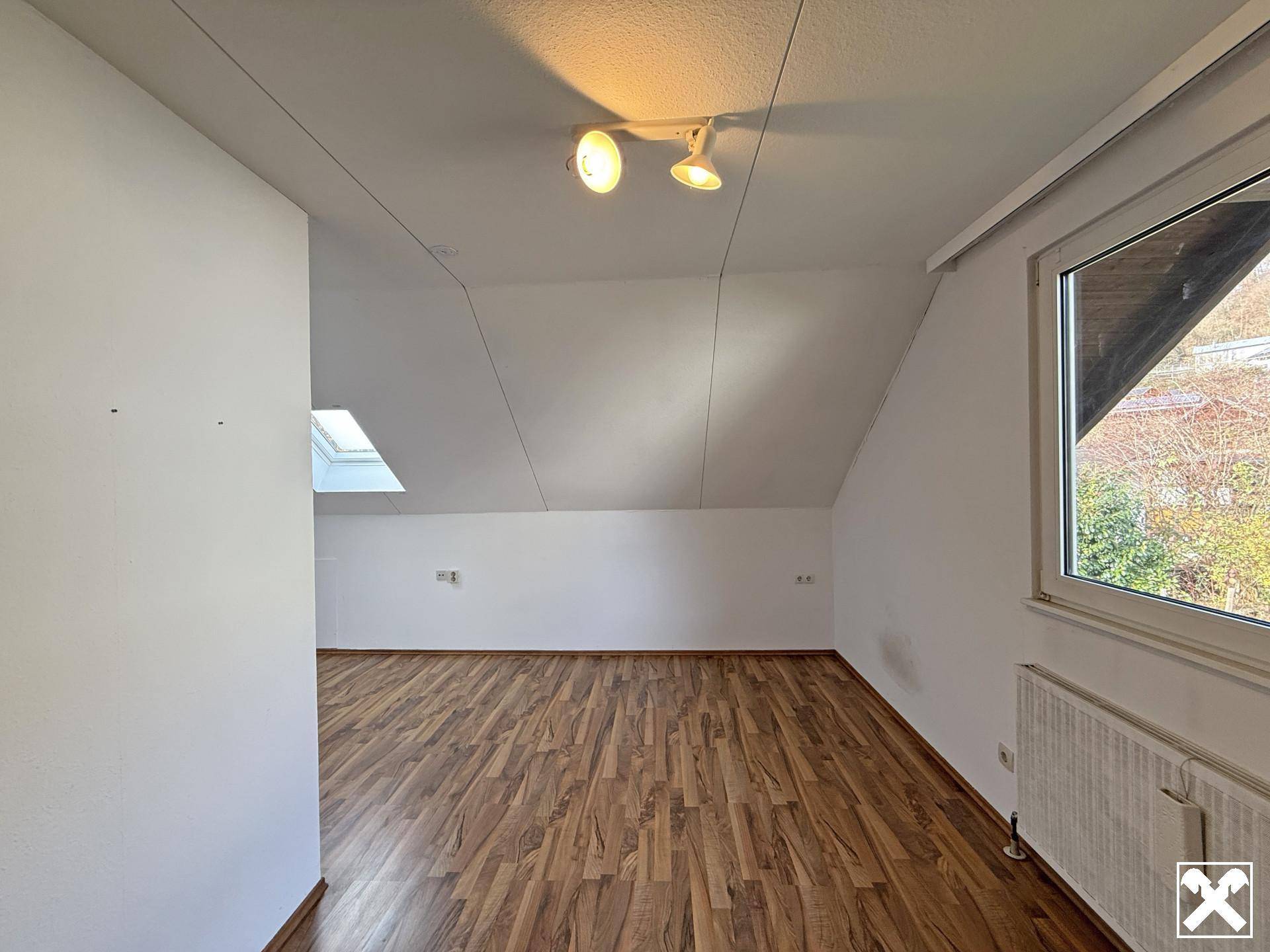 Helles Dachzimmer mit schräger Decke, Dachfenster und Laminatboden.
