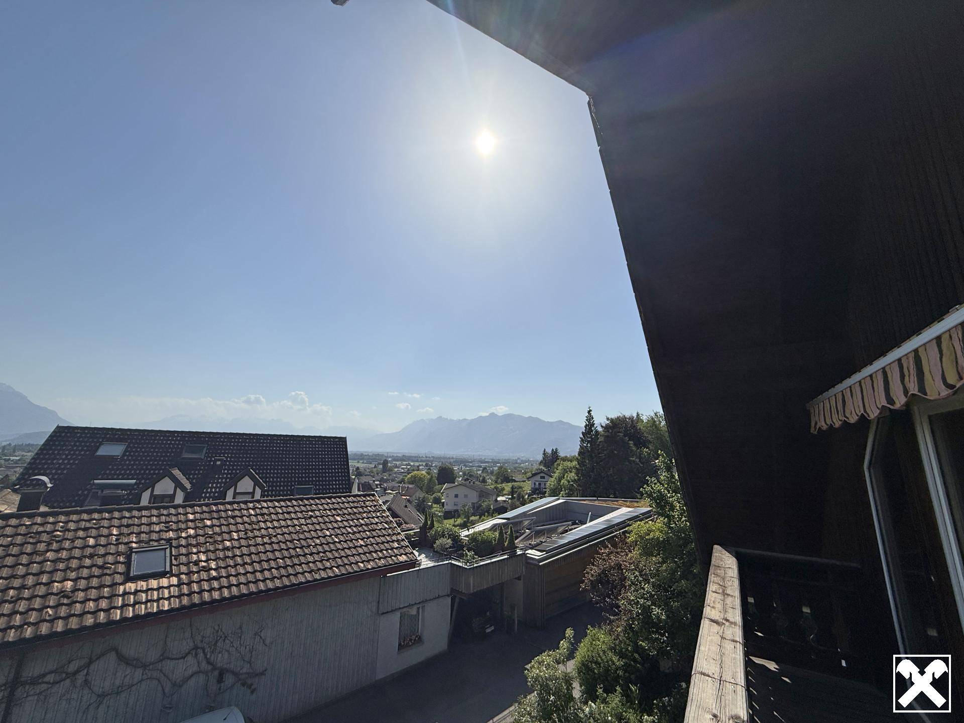 Sonniger Ausblick vom Balkon auf die umliegende Berglandschaft und die Dächer der Häuser.