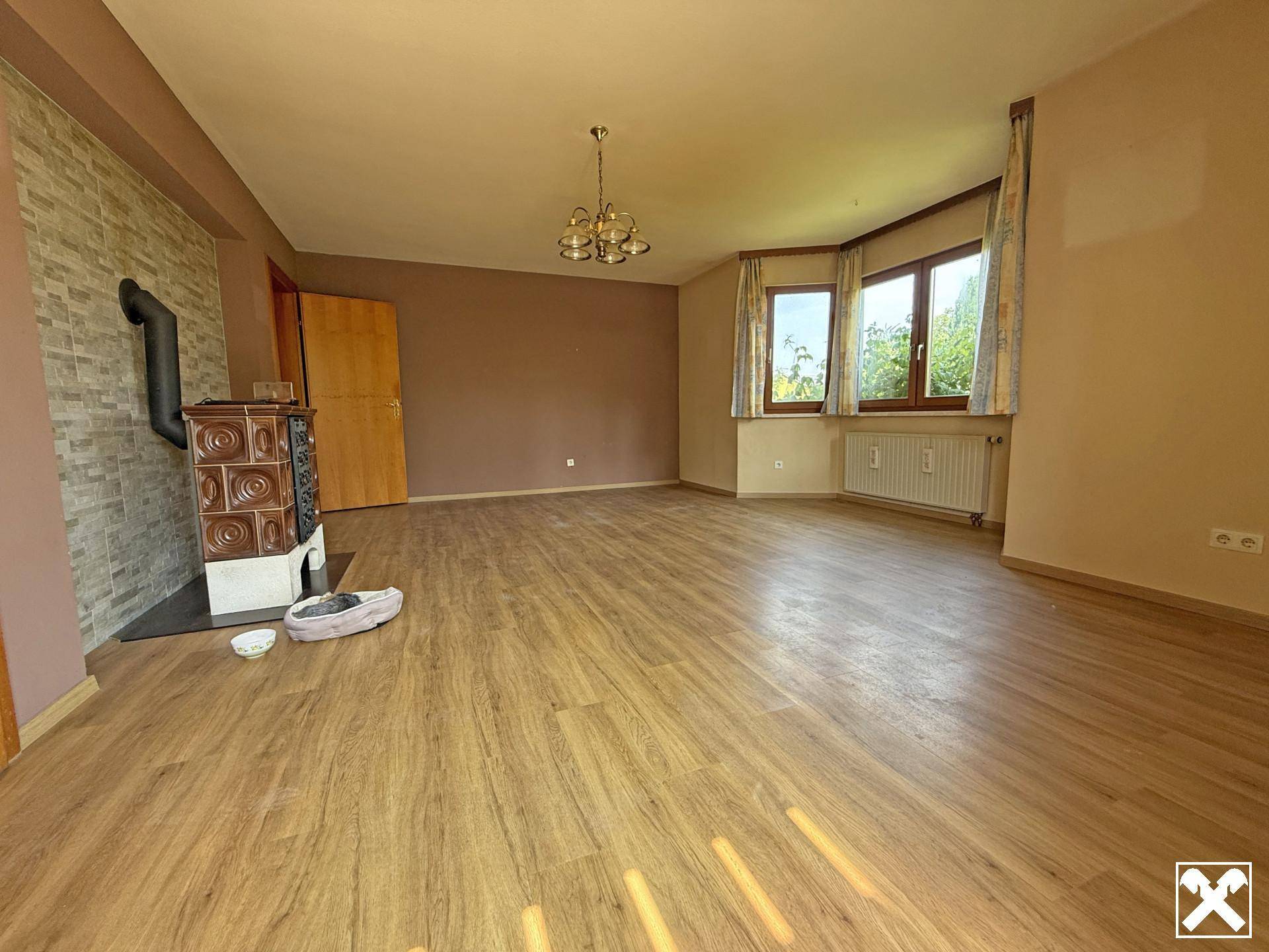Geräumiges Wohnzimmer mit Laminatboden, Kachelofen und Erkerfenstern.