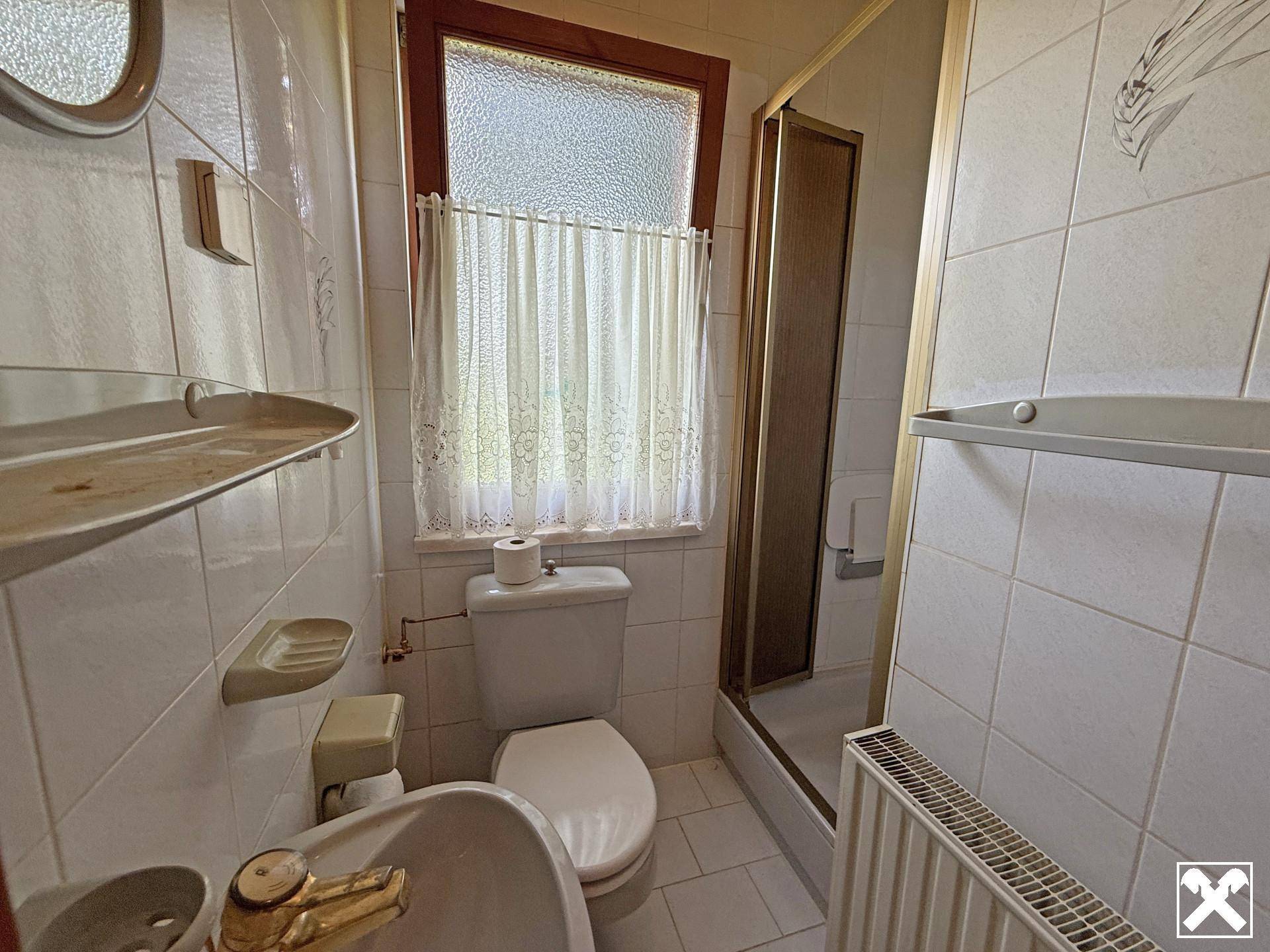 Kleines Badezimmer mit weißen Fliesen, Toilette, Waschbecken und Duschkabine.