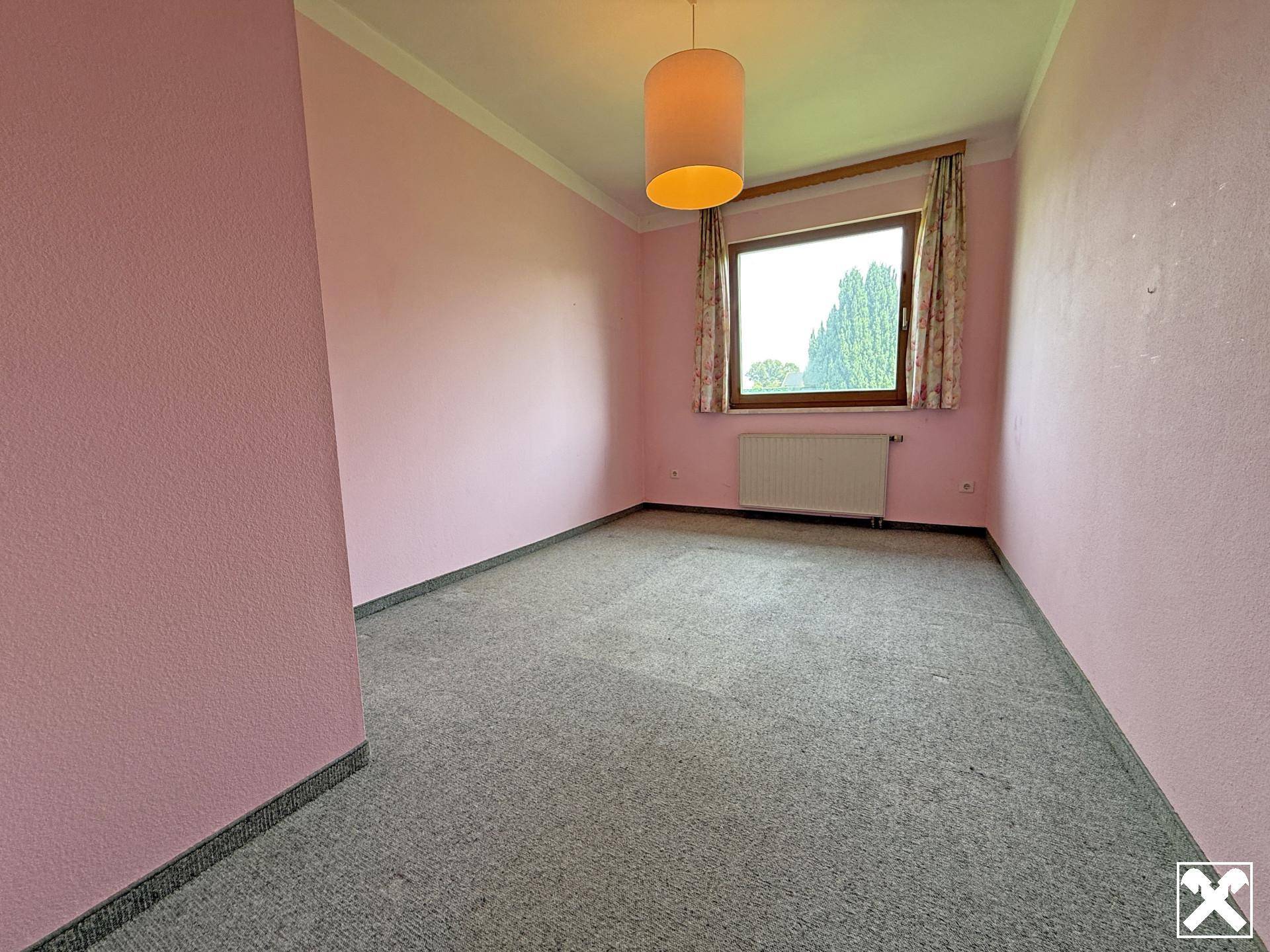 Schlafzimmer mit rosa Wänden, Teppichboden und Fenster mit Blick ins Grüne.