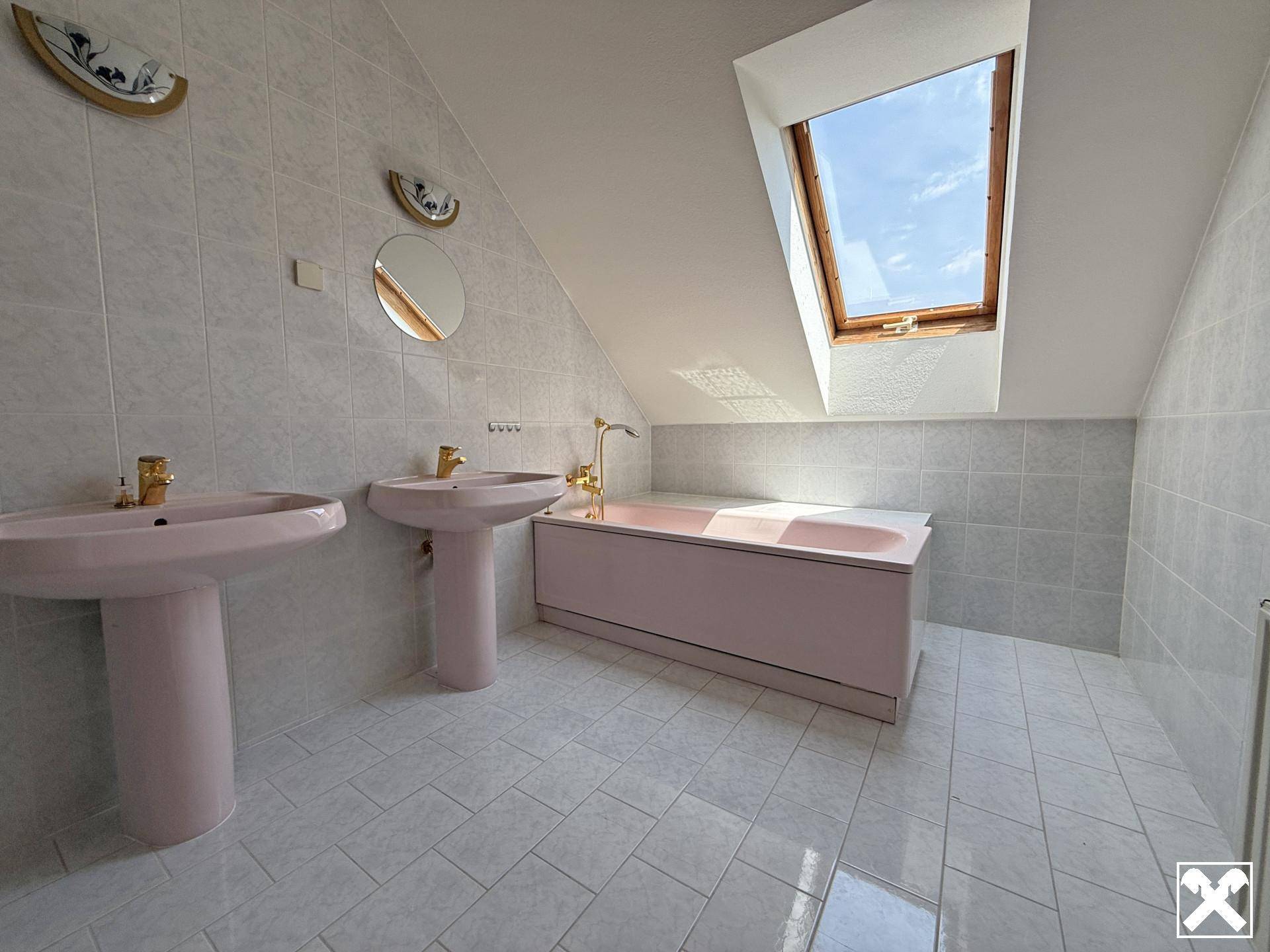Dachgeschoss-Badezimmer mit rosa Sanitärobjekten, Fliesenboden und Dachfenster.