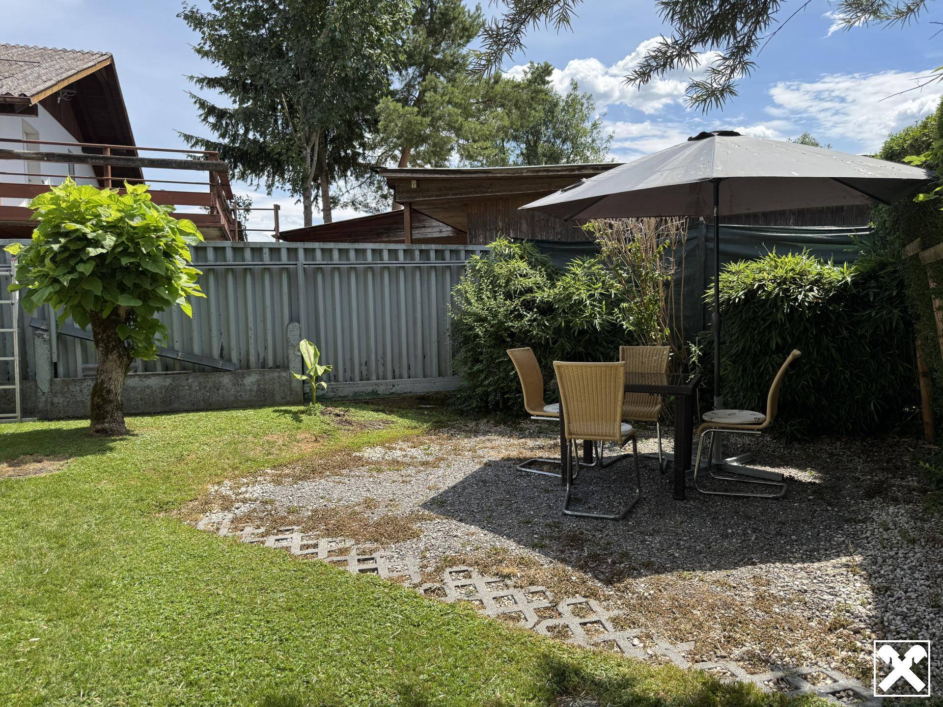 Gemütlicher Gartenbereich mit Sitzgelegenheiten und Sonnenschirm, umgeben von Grün.