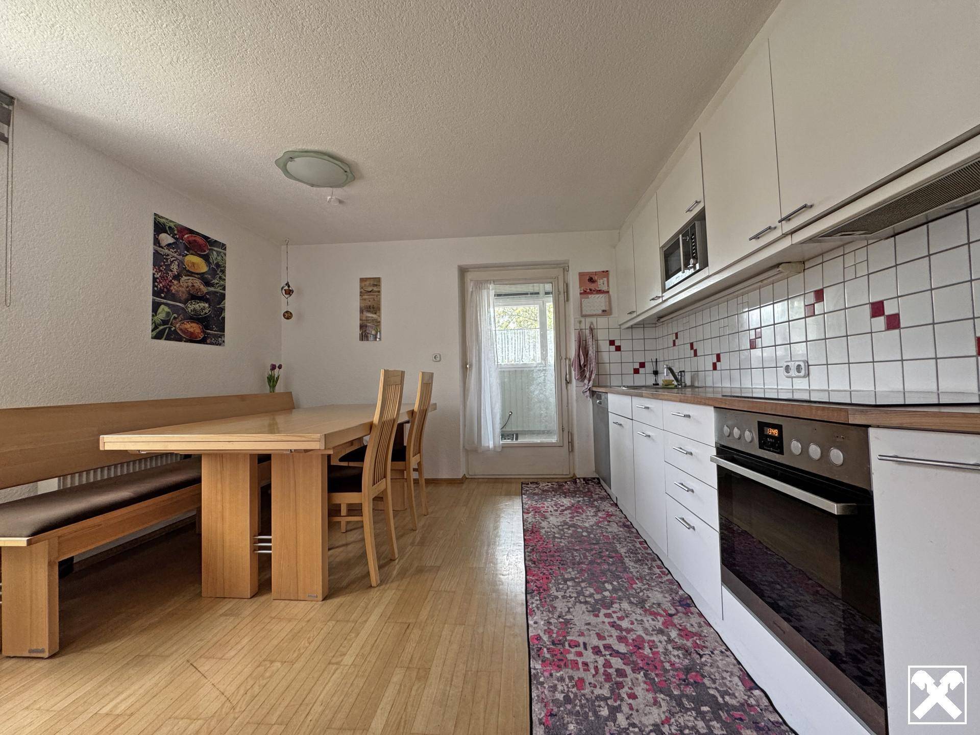Funktionale Wohnküche mit Holztisch, Sitzbank und weißen Einbauschränken mit Holzarbeitsplatte.