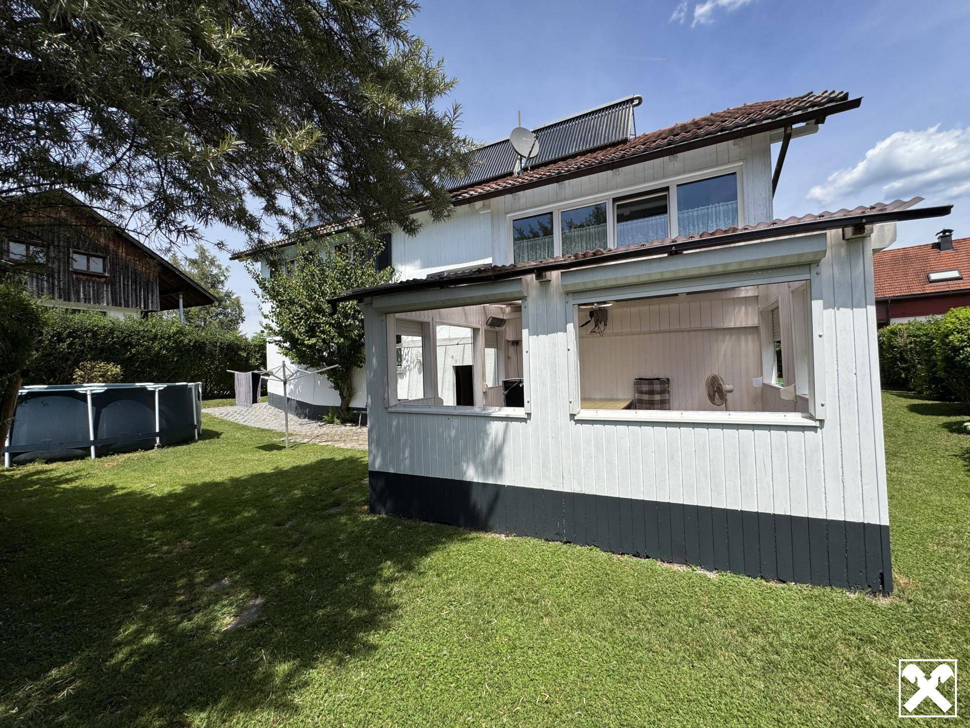 Rückseite des Hauses mit Wintergarten, Rasenfläche und einem Aufstellpool im Garten.