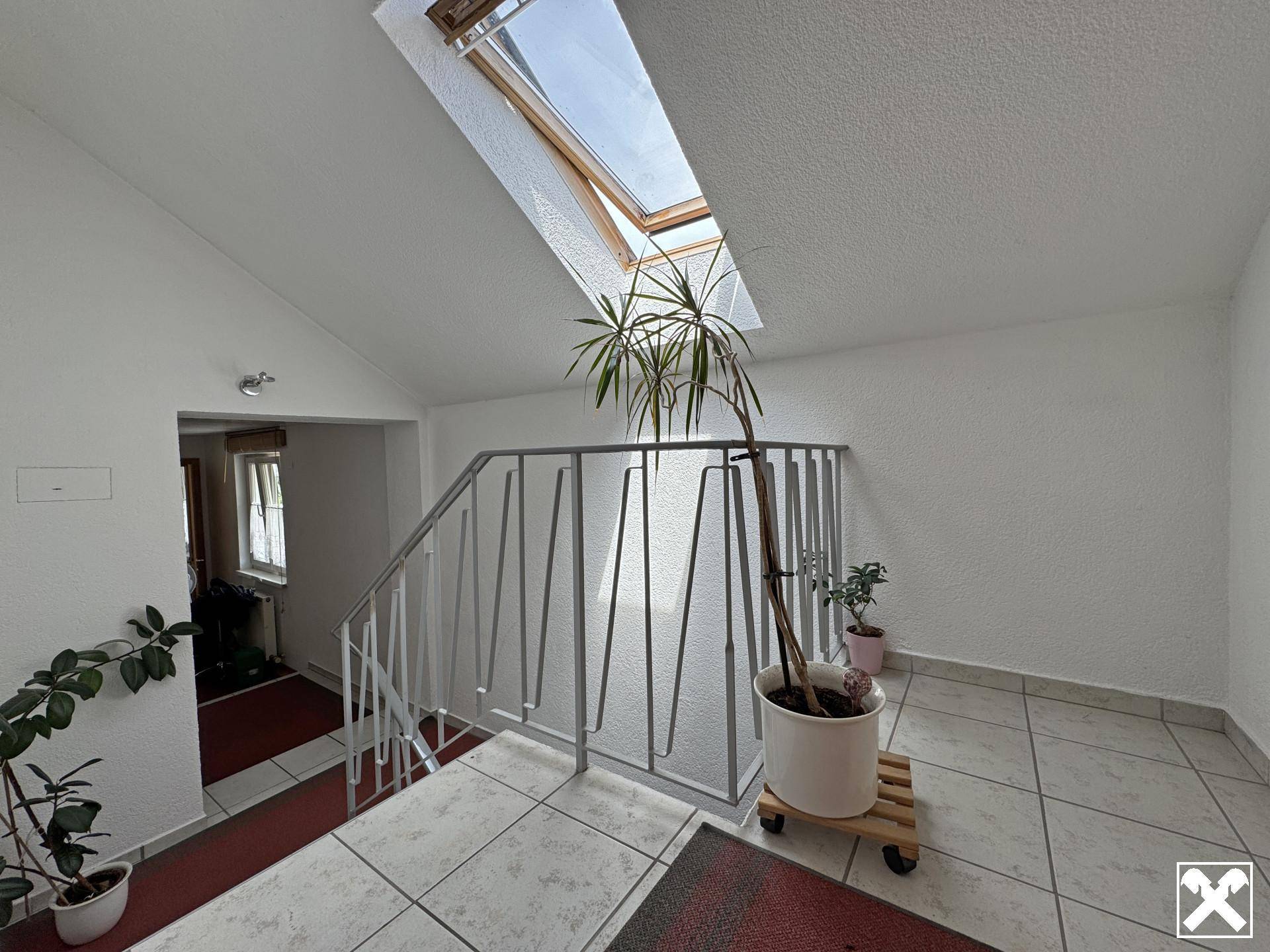 Oberer Treppenbereich mit Fliesenboden, Pflanzen und viel Tageslicht durch ein großes Dachfenster.