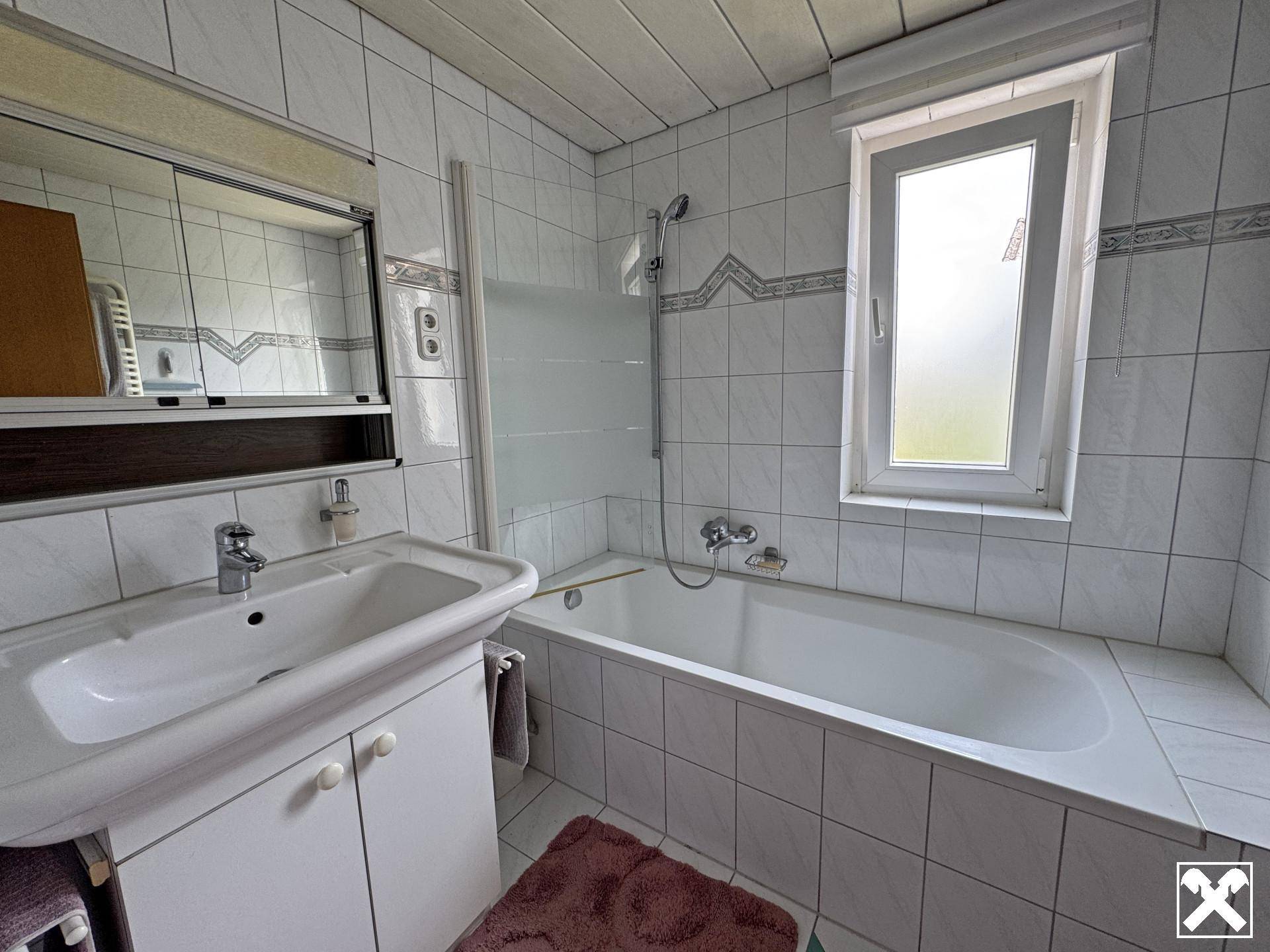 Gefliestes Badezimmer mit Badewanne, Waschbecken und Fenster, in gutem, gepflegtem Zustand.