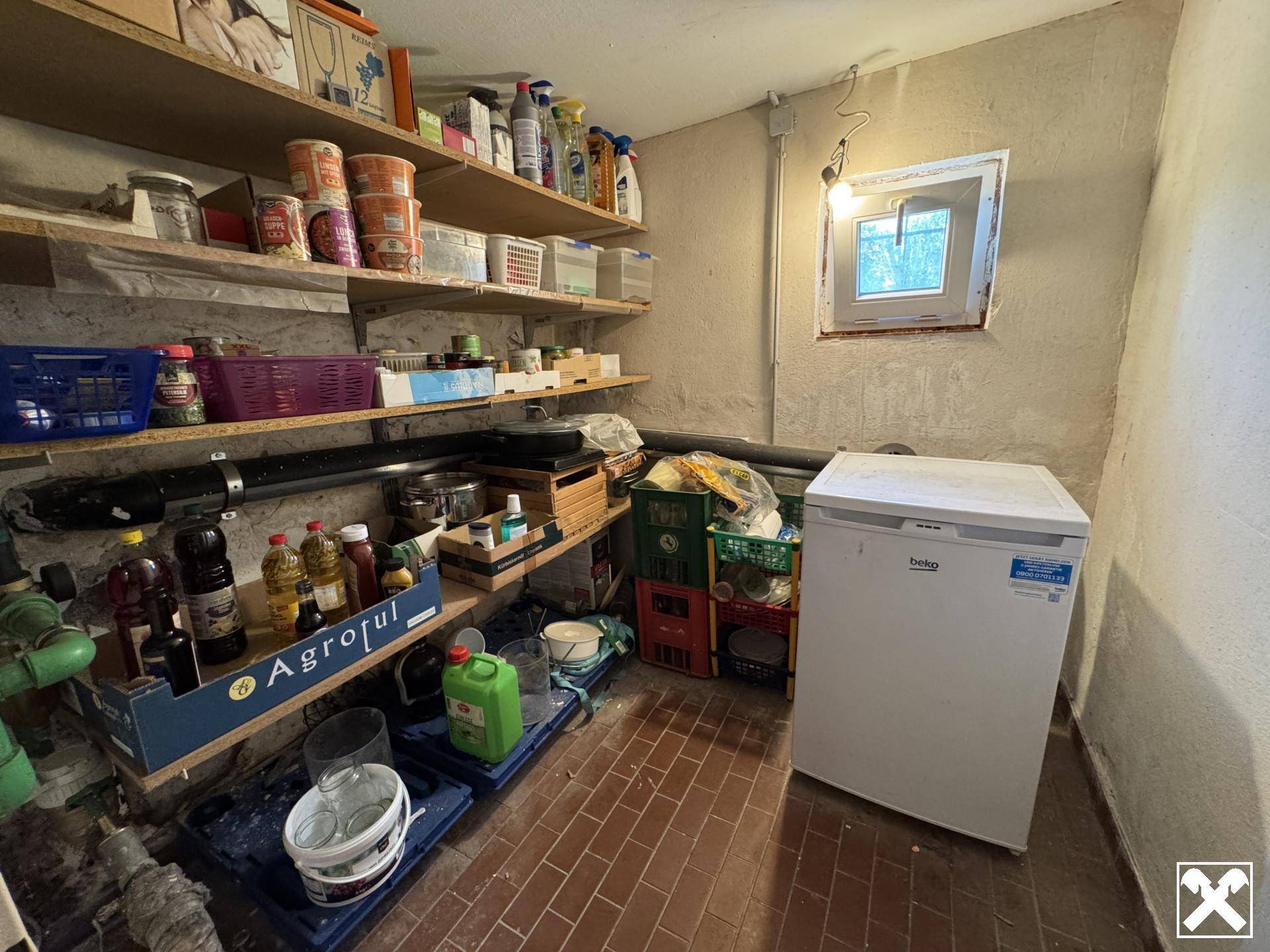 Praktischer Abstellraum im Keller mit Regalen, Gefrierschrank und kleinem Fenster.