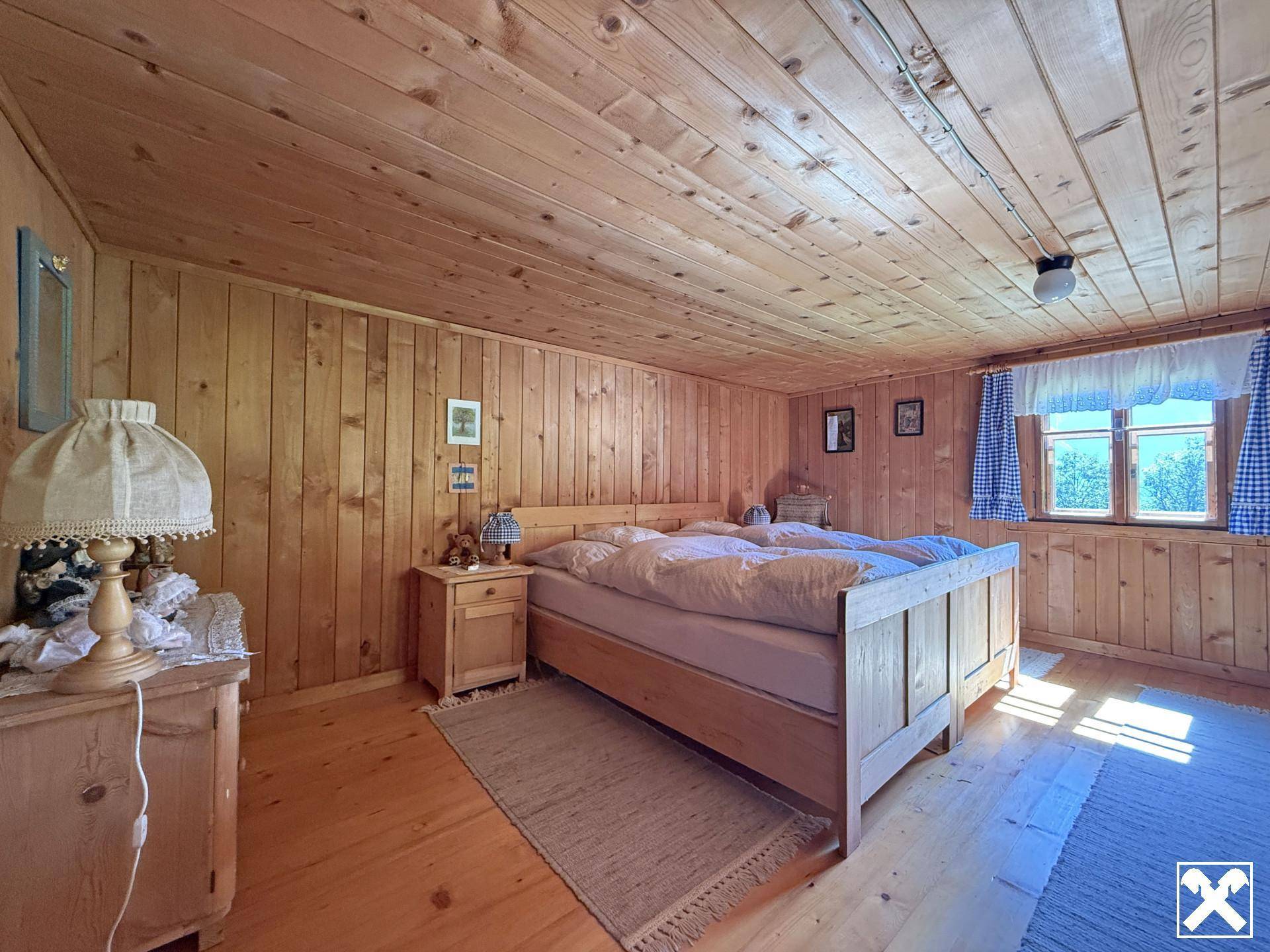 Helles Schlafzimmer mit Holztäfelung, Doppelbett und traditionellen Vorhängen, durchflutet von Sonnenlicht.