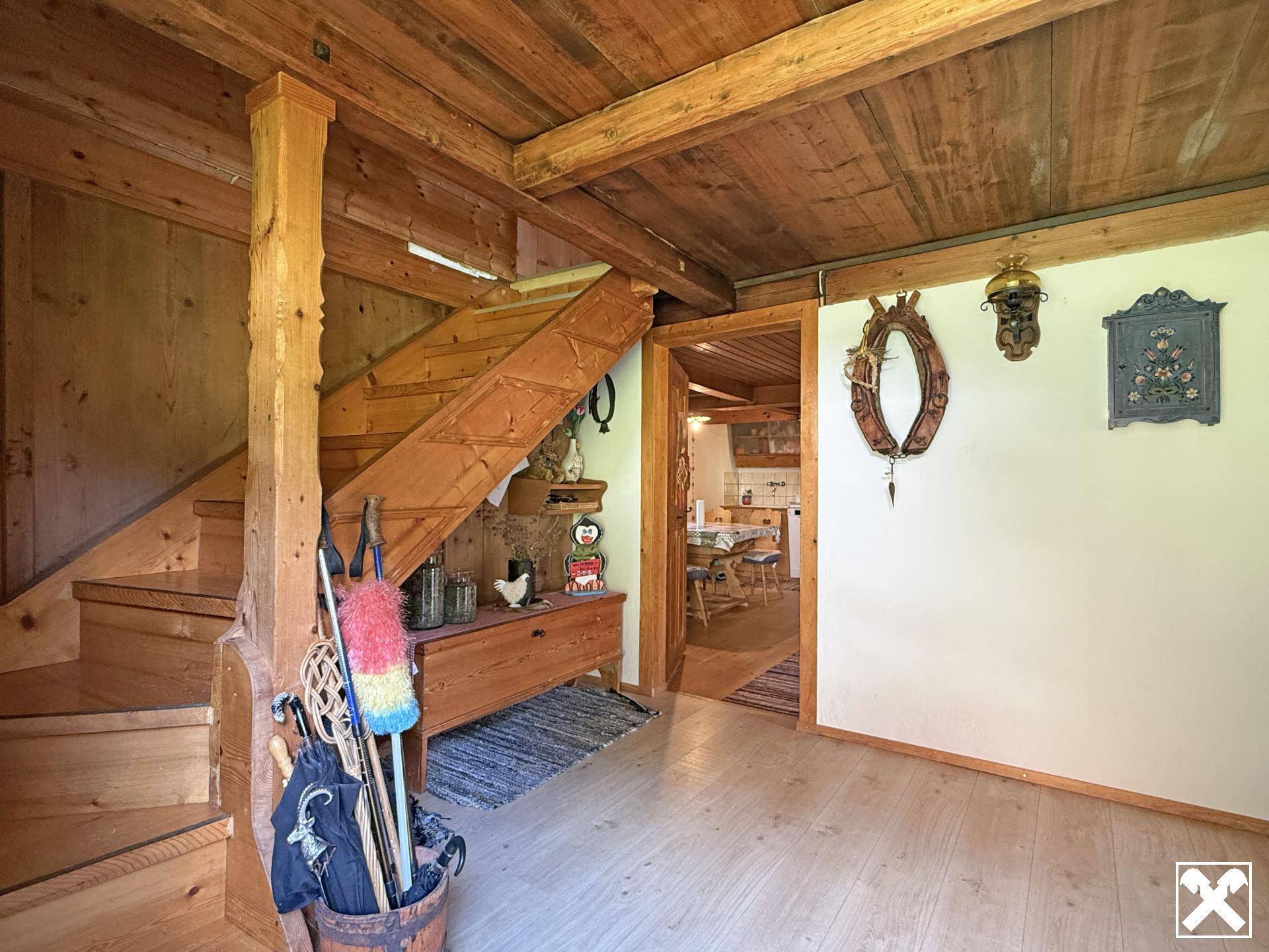 Rustikaler Flur mit Holztreppe, Holzbalkendecke und Zugang zu weiteren Räumen.